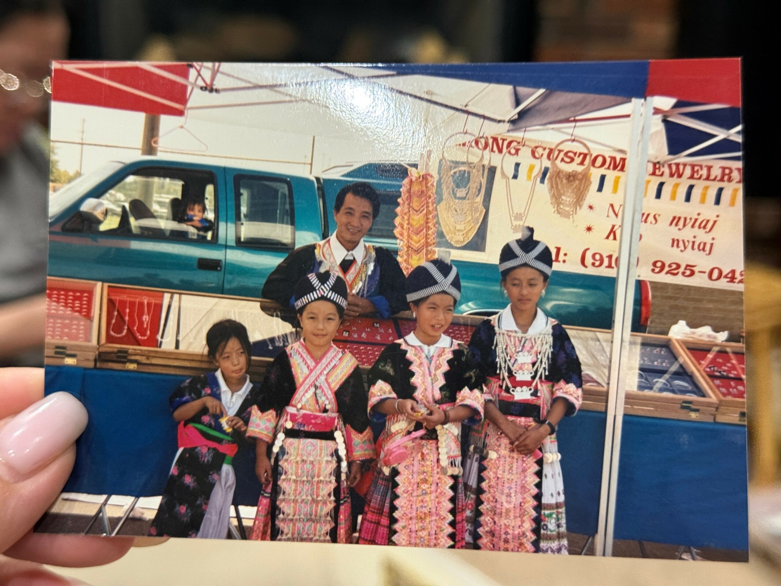 Group of five people in traditional clothing standing in front of a vehicle at a fair or festival.