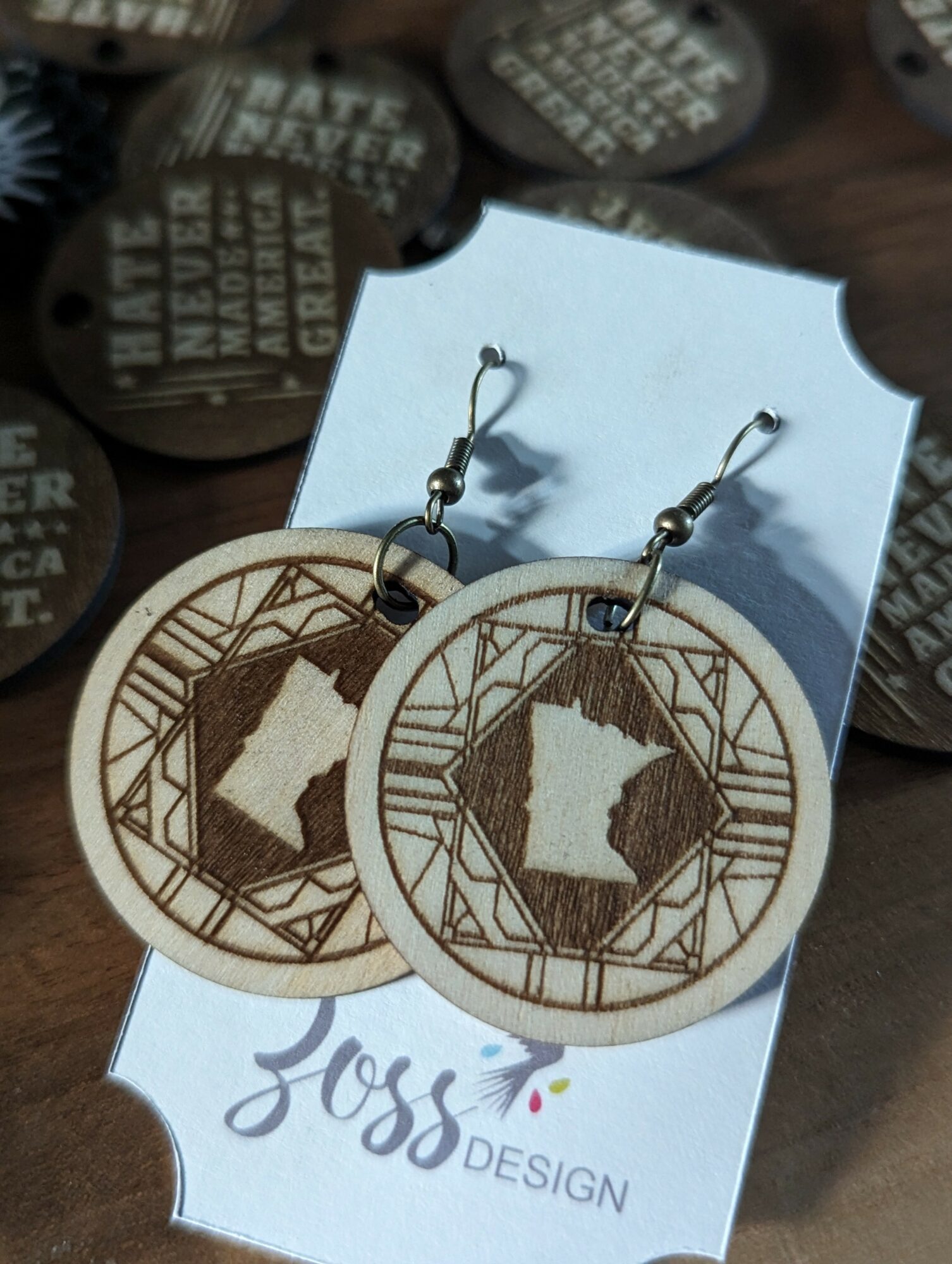 Wooden earrings with a circular design featuring the outline of a state and geometric patterns, displayed on a white card.