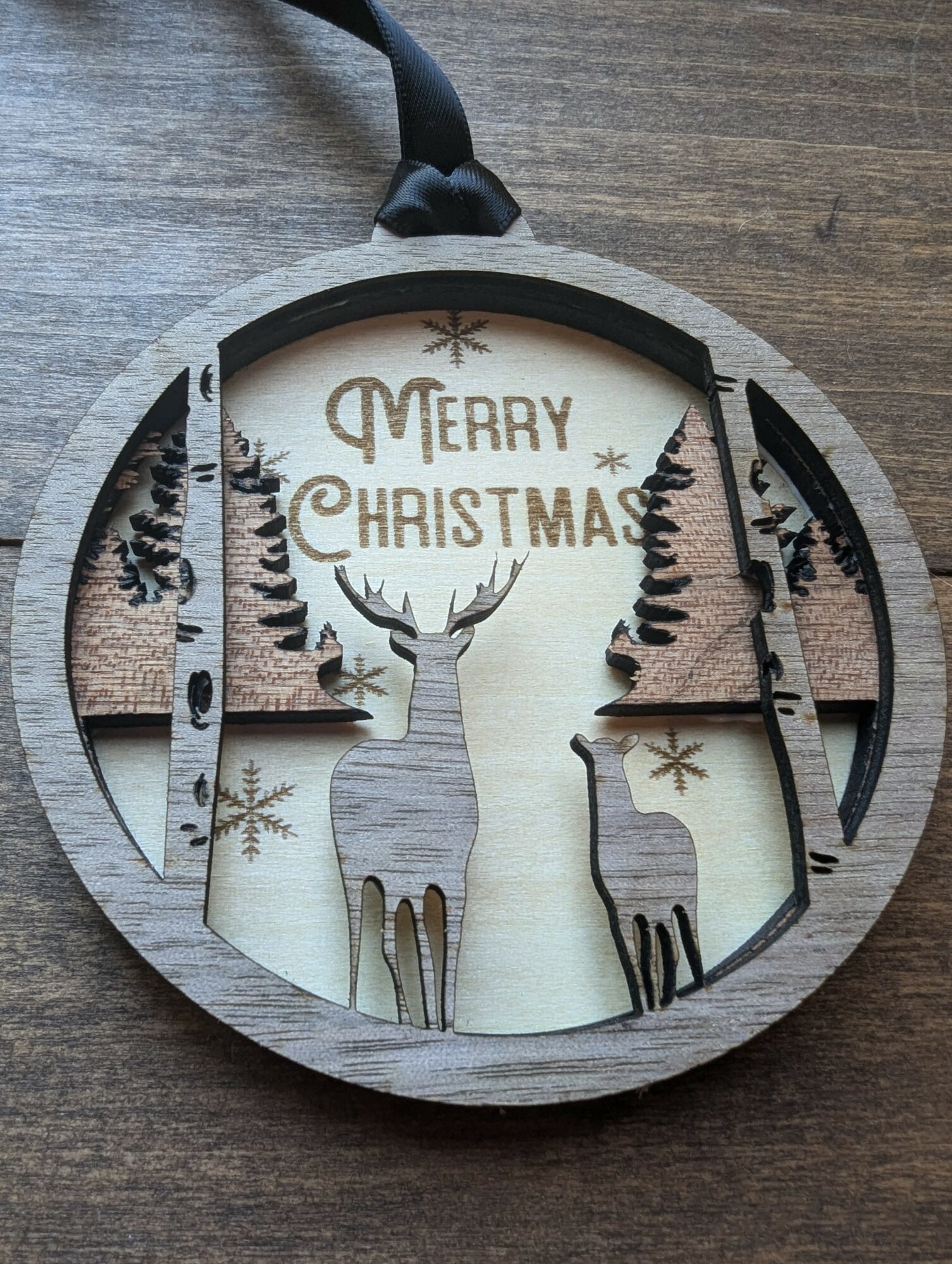 Decorative Christmas ornament with reindeer and trees, displaying 'Merry Christmas' text, on a wooden surface.