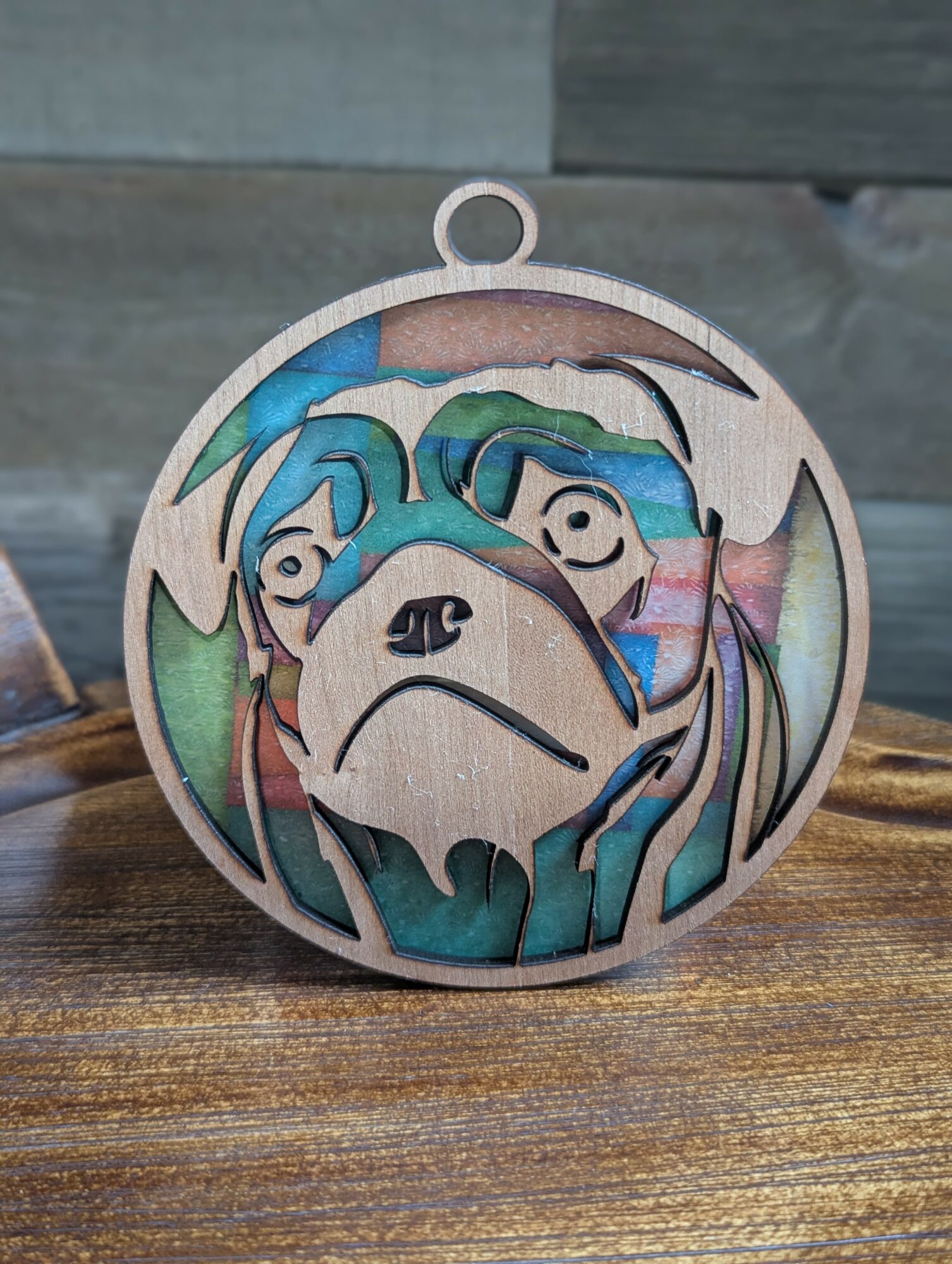Colorful circular ornament featuring a stylized dog and two people, with a loop at the top for hanging.