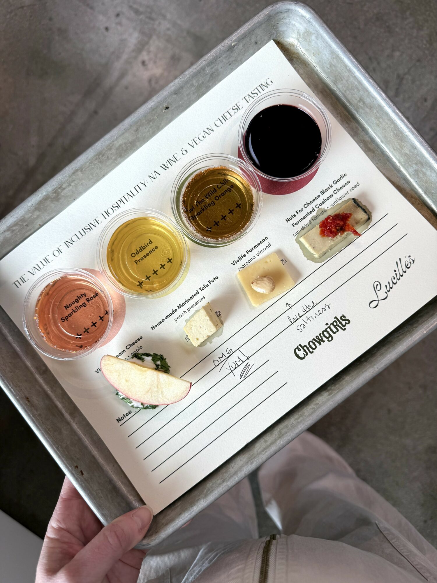 Tray with three small cups of different sauces, a slice of cheesecake, and a dessert with berries, on a paper sheet.