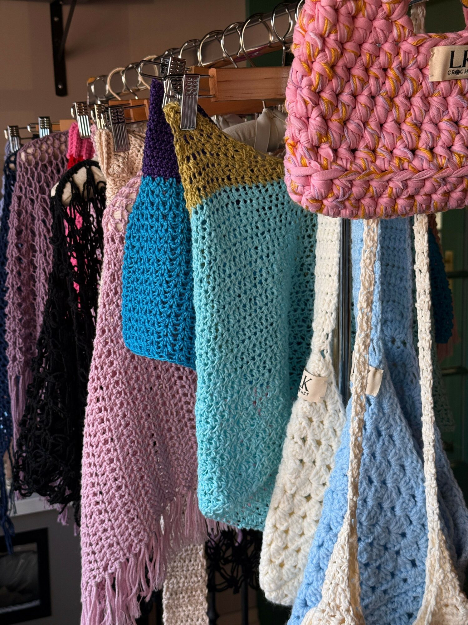 Stack of colorful crocheted or knitted fabric pieces in pink, yellow, blue, white, and black, hanging on a rack.