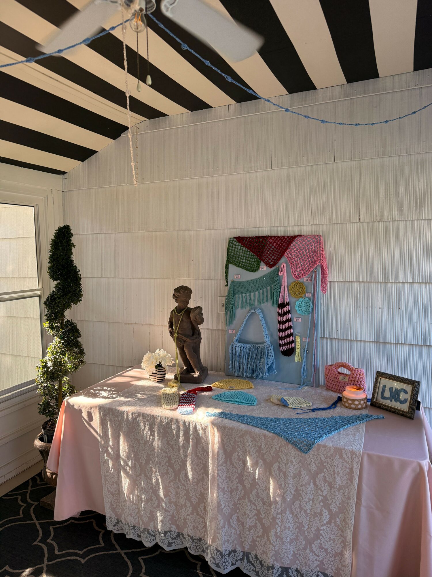 Child standing near a table with a pink tablecloth, decorated with a cake and party items, against a white wall.