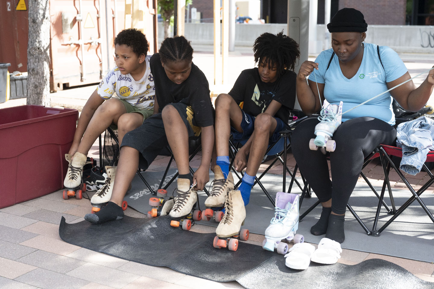 Four people sit on chairs with roller skates, preparing to skate outdoors on a sunny day.