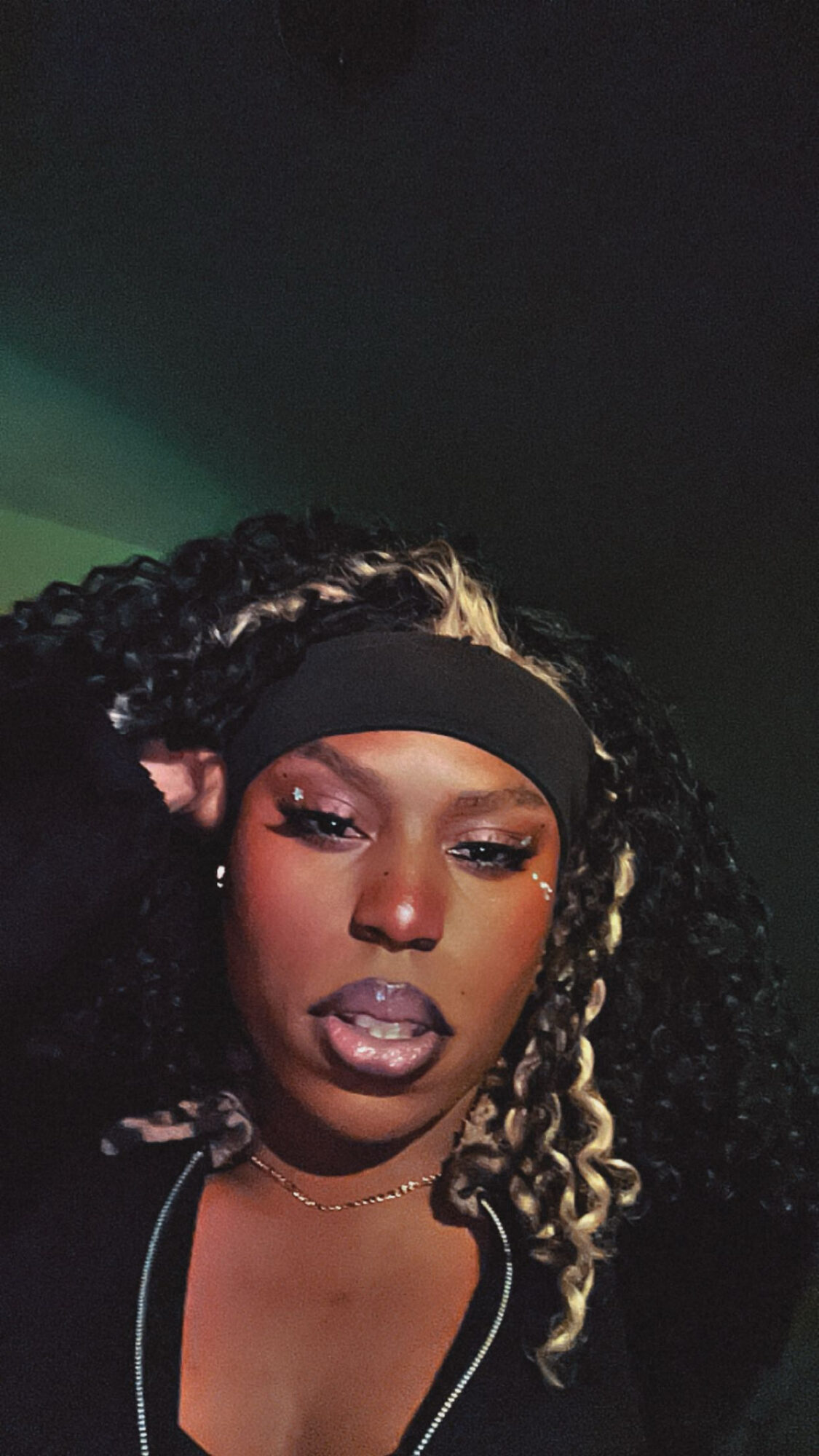Close-up of a woman with curly hair, wearing a headband and makeup, looking at the camera.