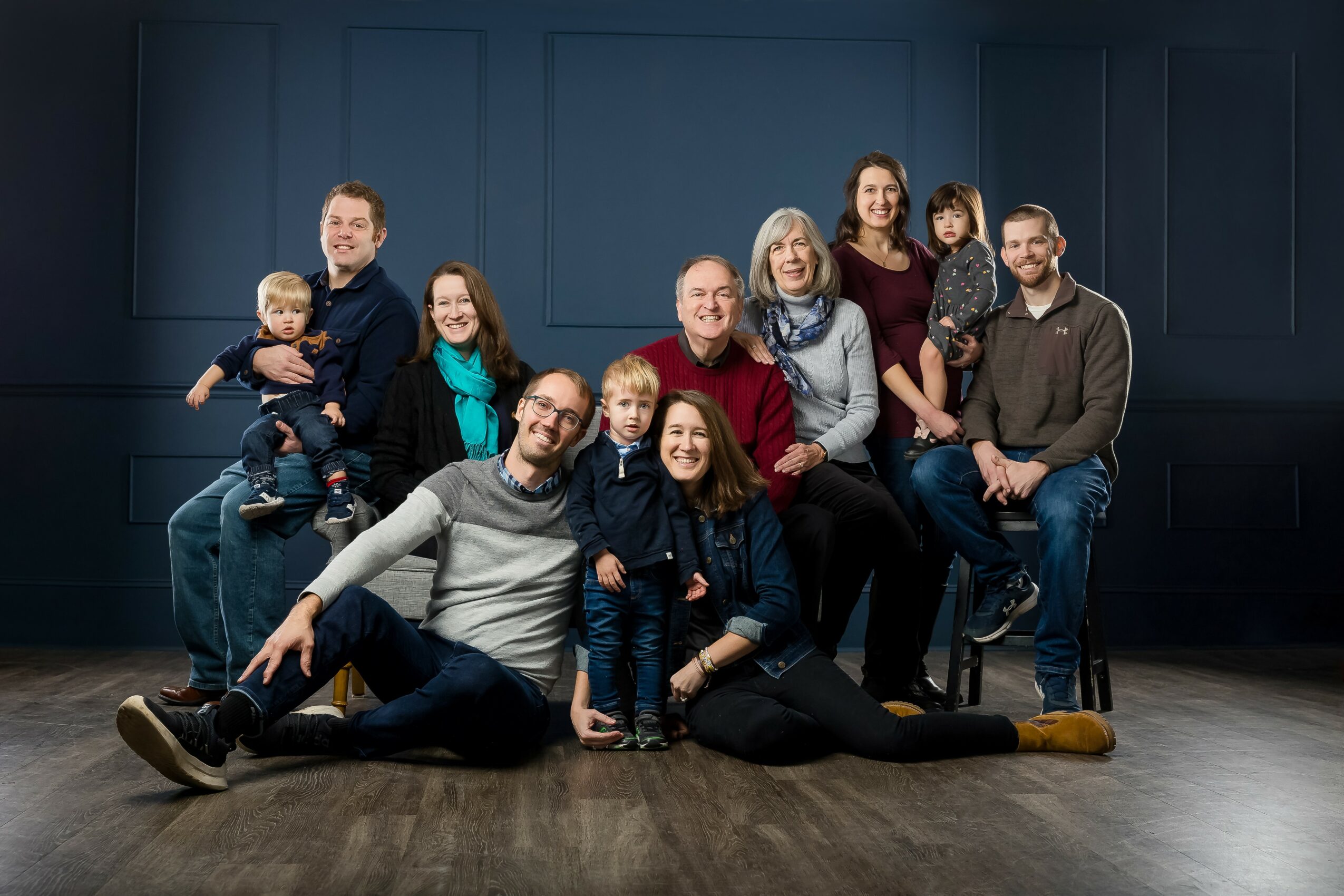 Group of ten people, including children, posing together indoors against a dark wall, smiling and sitting or standing.
