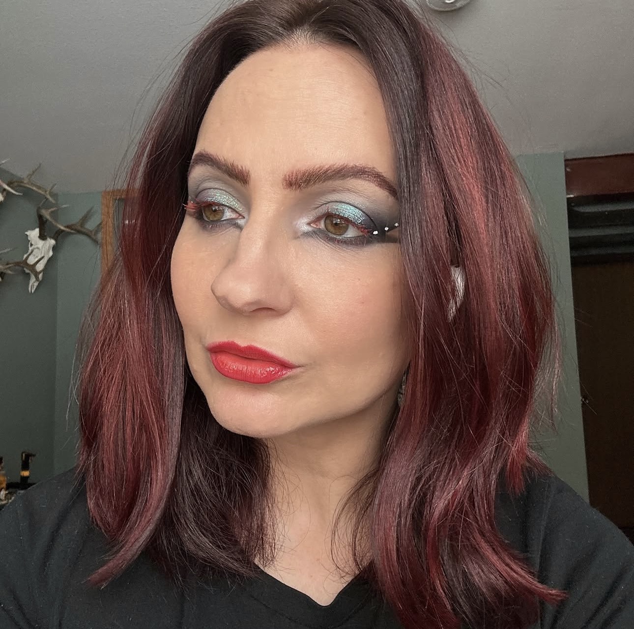 Woman with makeup and shoulder-length reddish-brown hair looking to the side in a room.