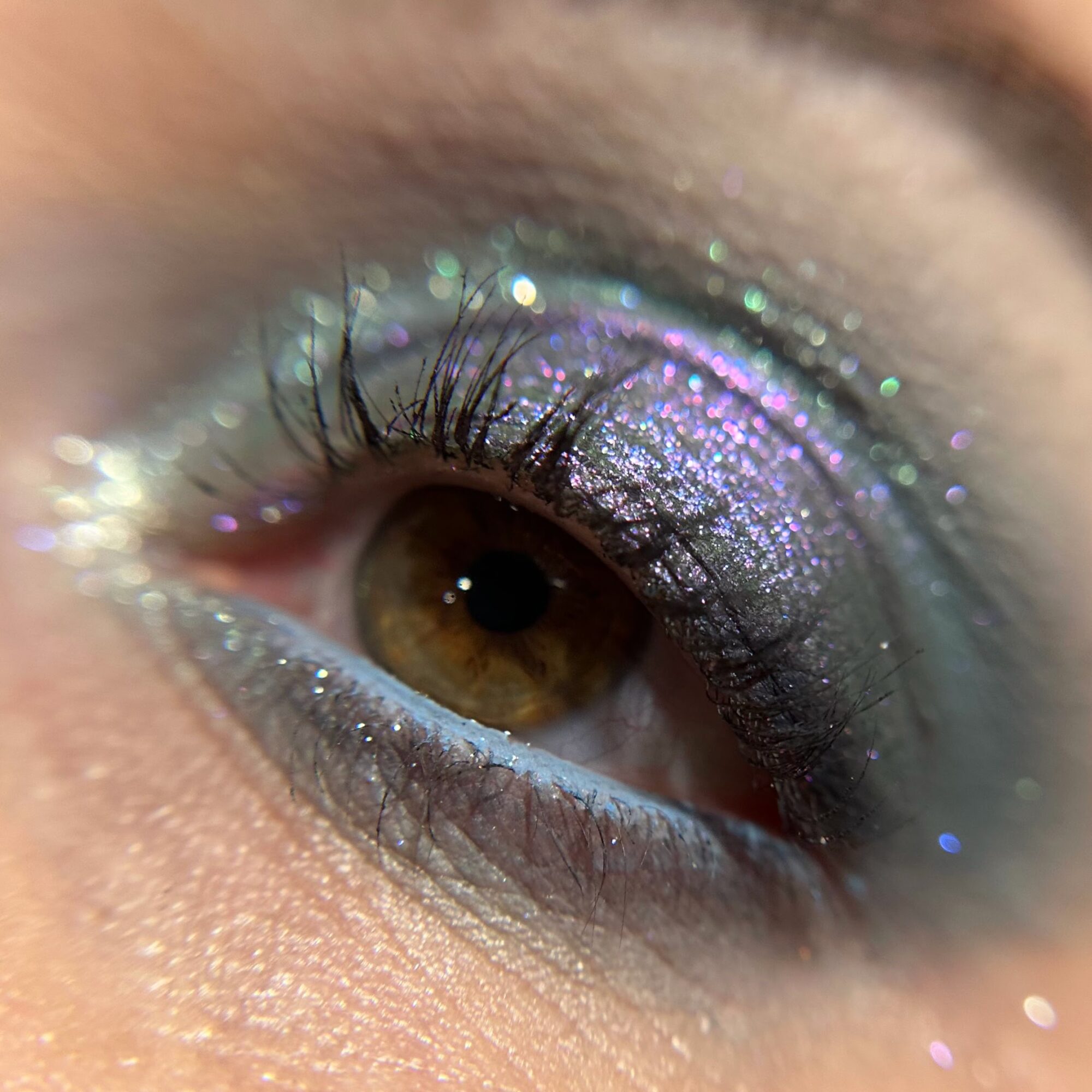 Close-up of a person's eye with colorful, glittery eyeshadow and long eyelashes.