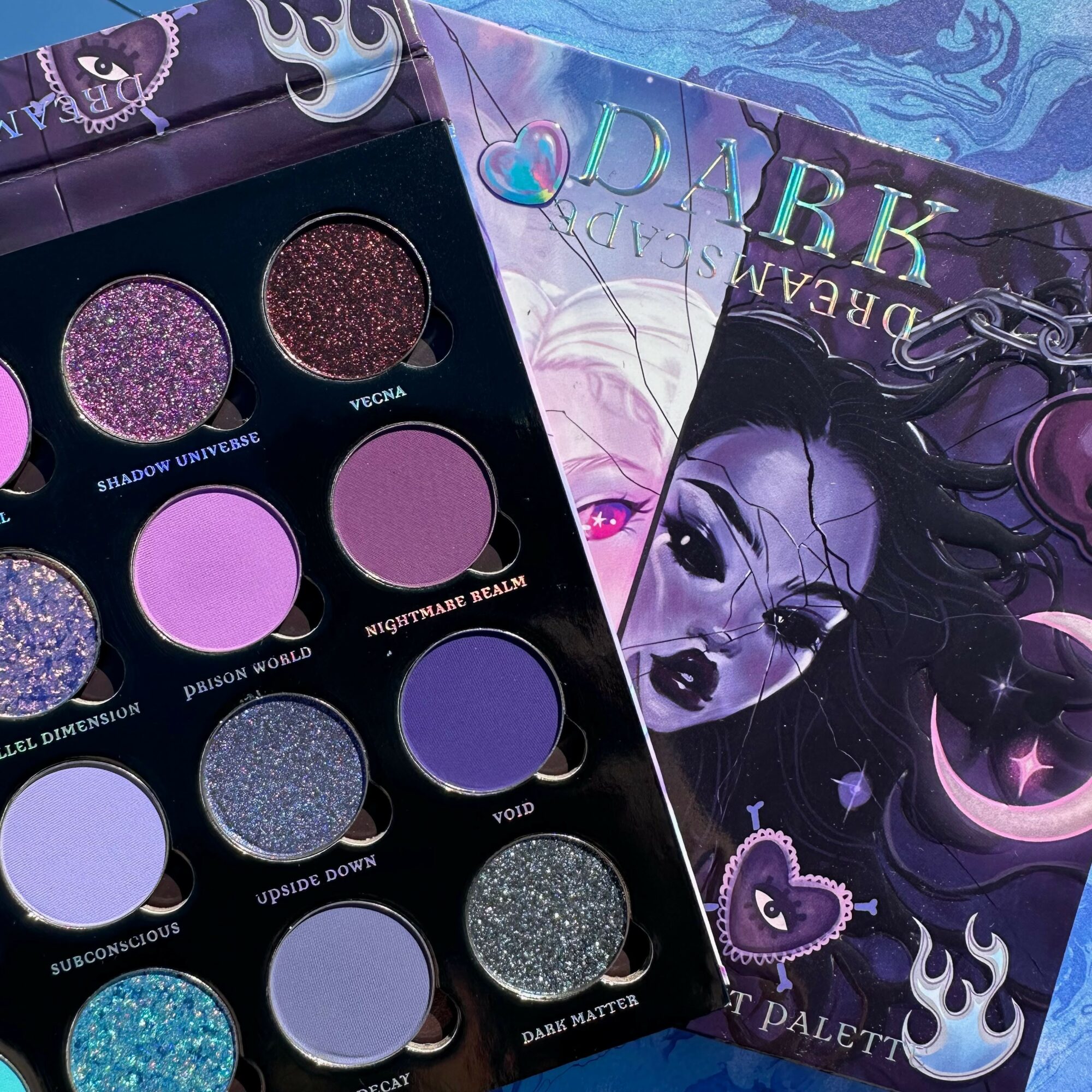 Eyeshadow palette with nine purple and blue shades, and a dark illustrated book cover with a female character and moon.