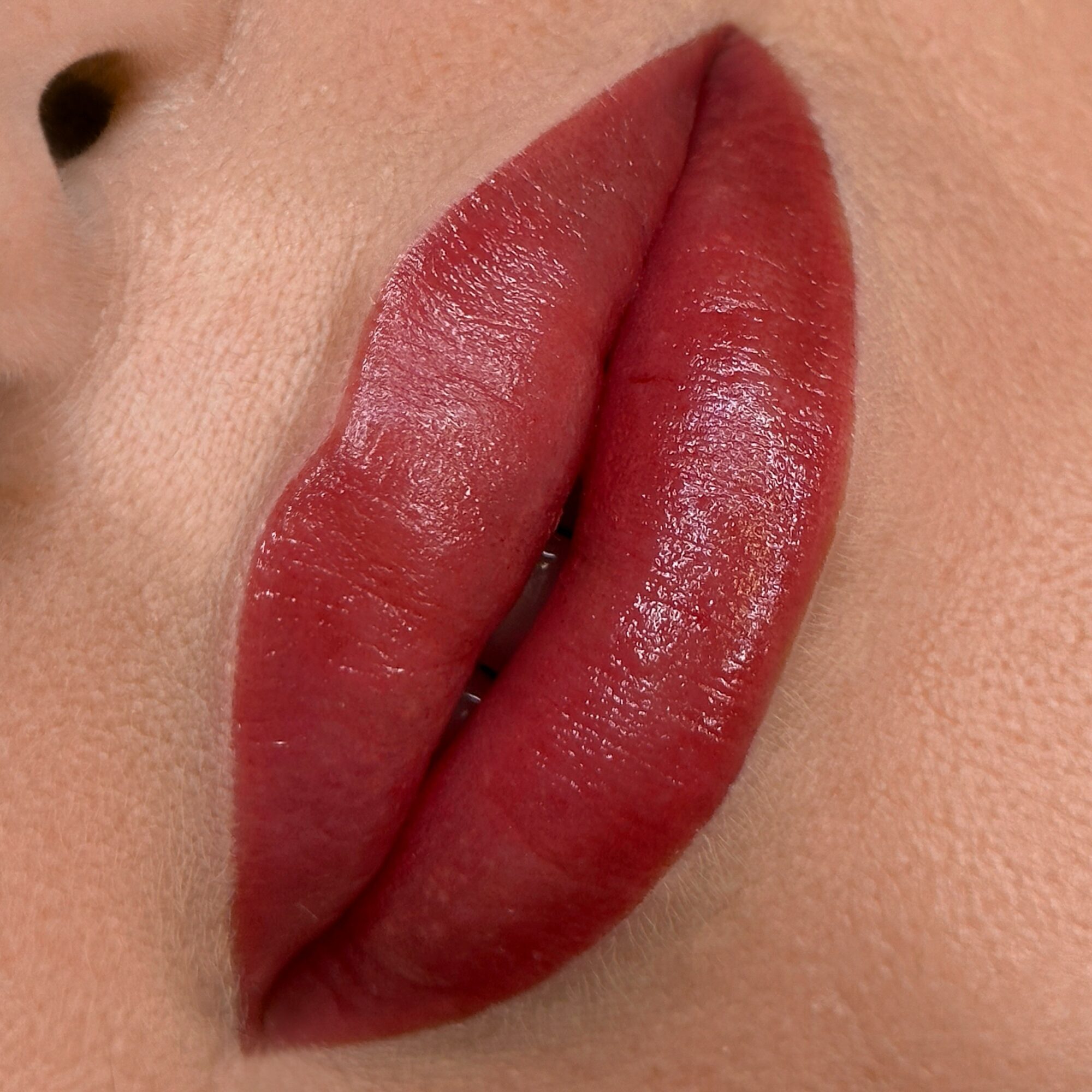 Close-up of lips with red lipstick, showing smooth texture and natural skin around.