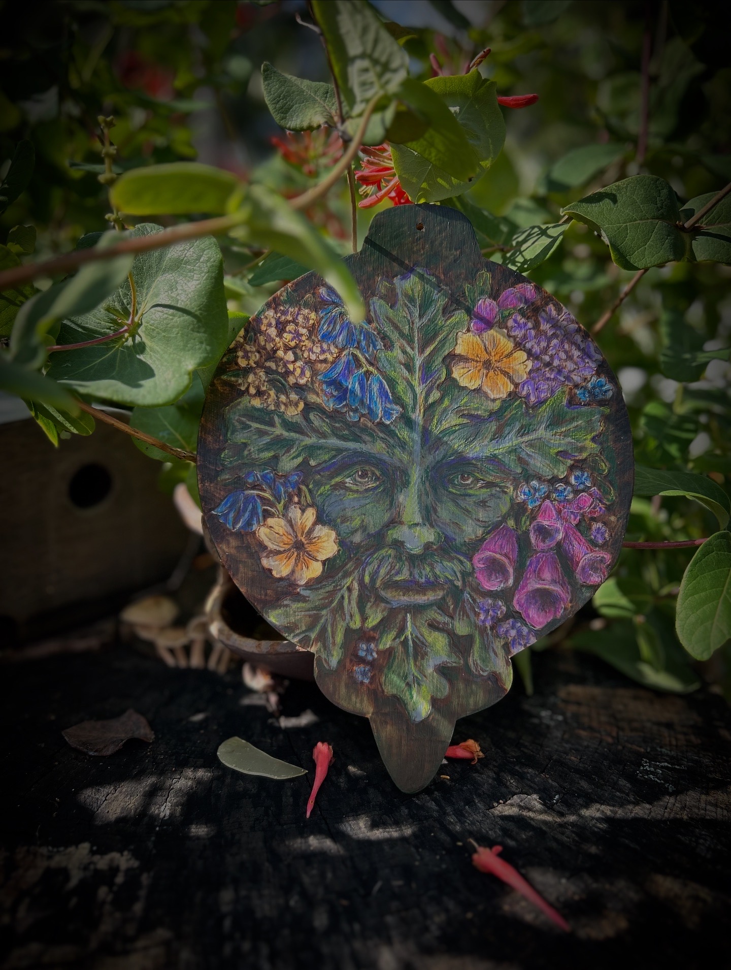 Leaf with colorful floral and butterfly design, surrounded by green leaves and plant stems.