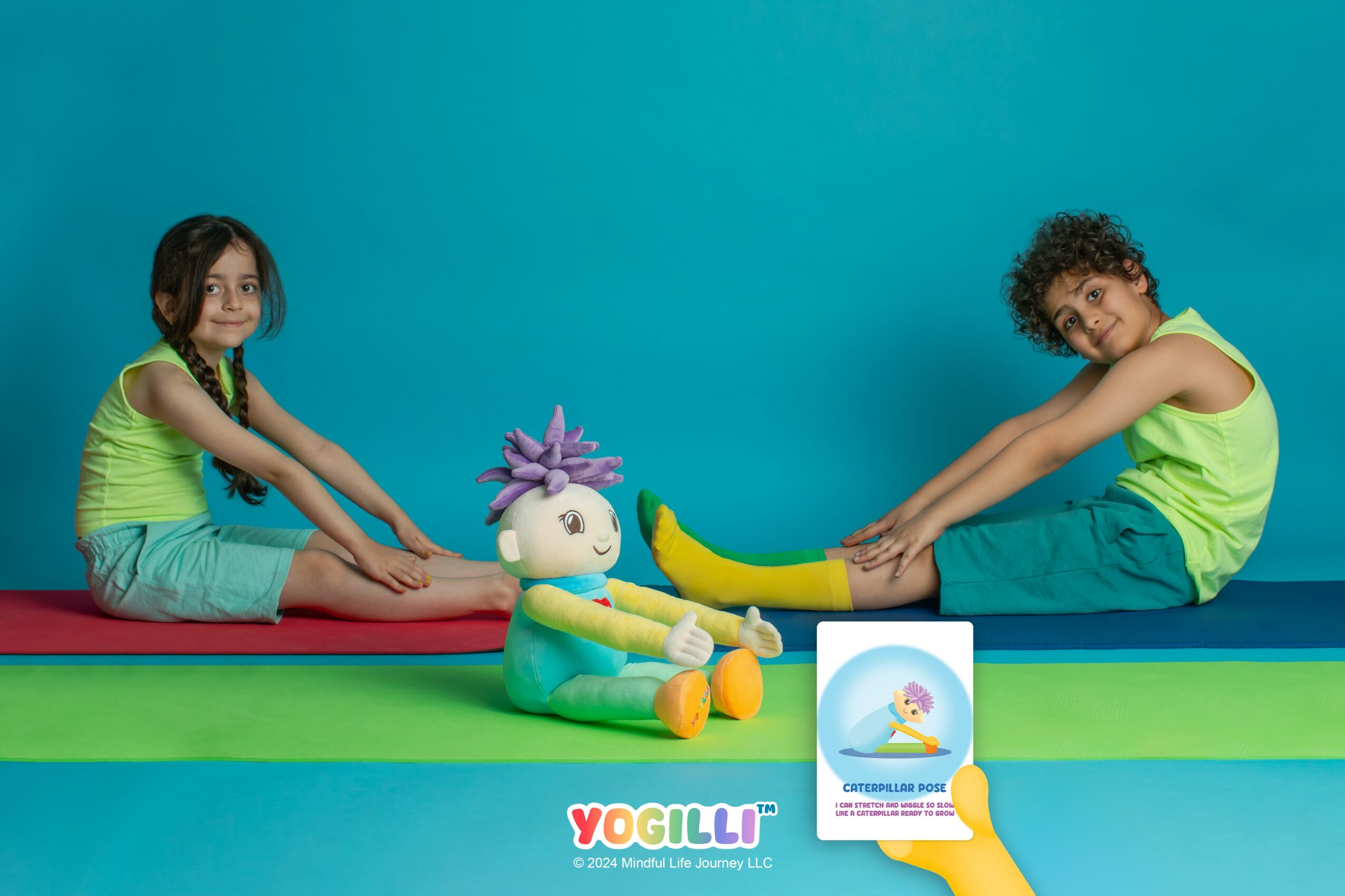 Two children in green shirts sit on a colorful mat with a plush doll between them, against a blue background.