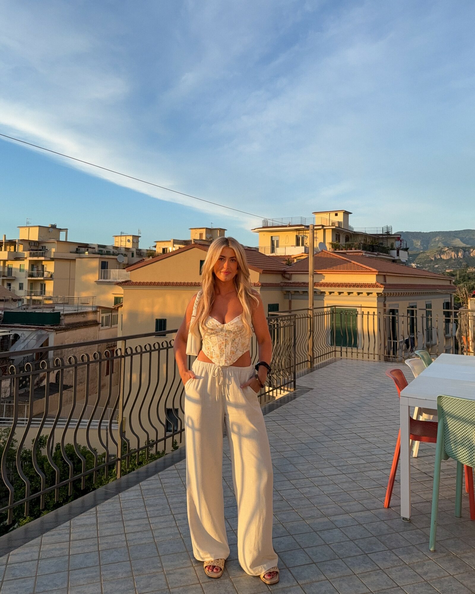 Woman standing on a rooftop terrace with buildings and a blue sky in the background.