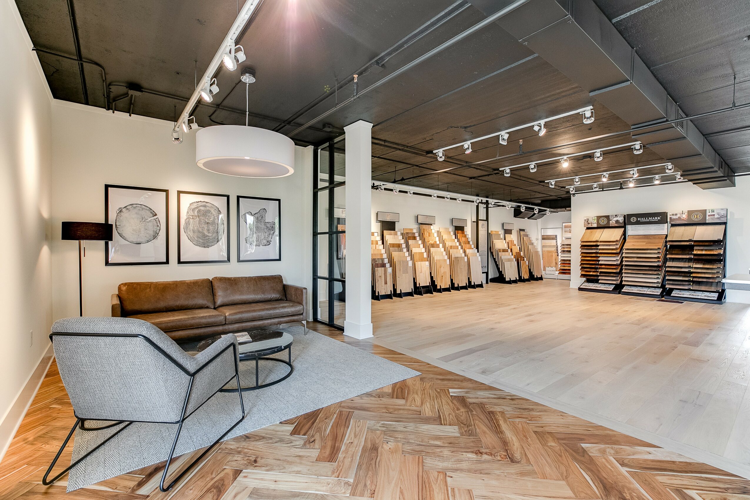 Furniture store interior with sofa, armchair, framed artwork, and display of flooring samples, well-lit with modern decor.