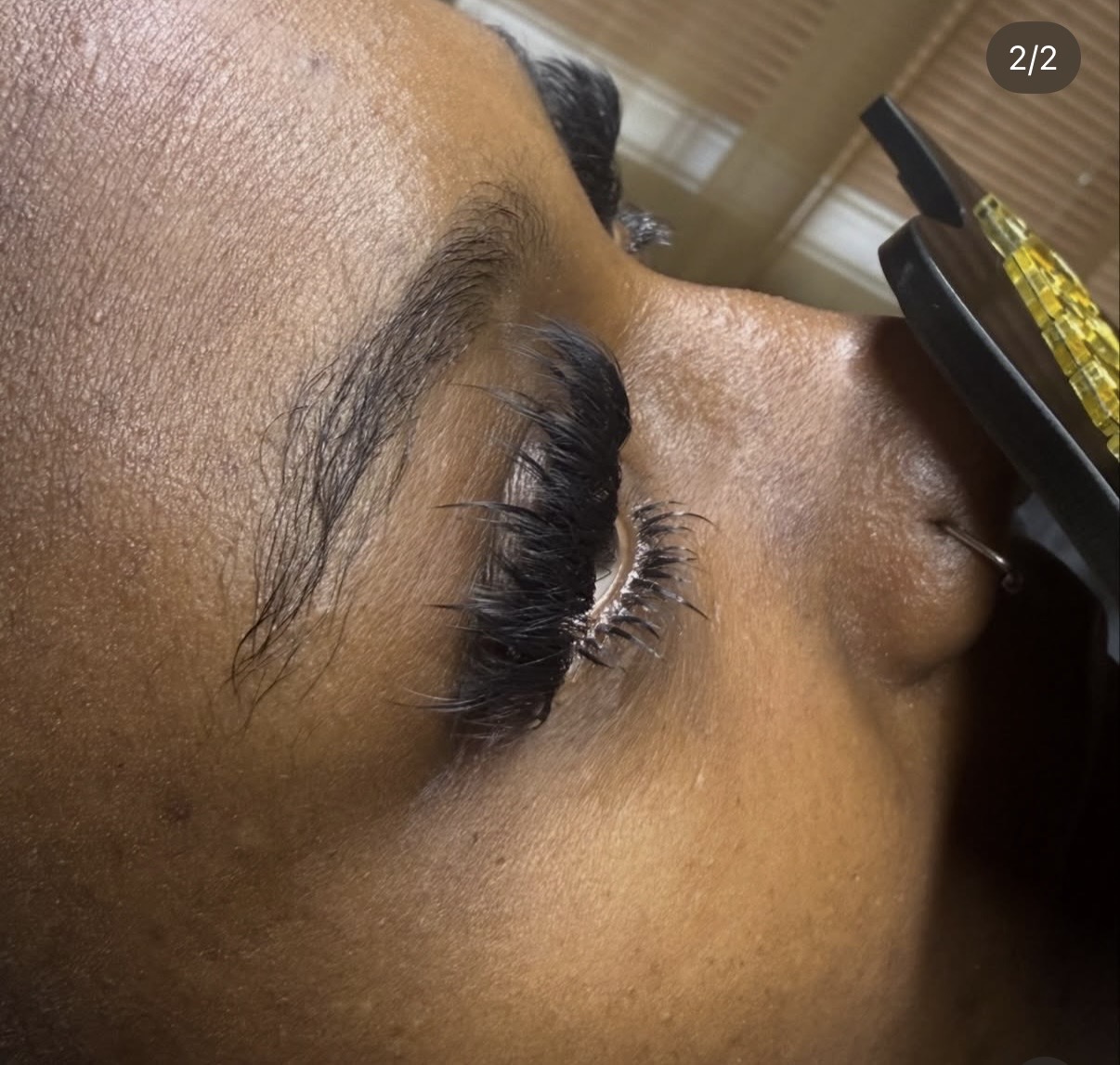 Close-up of a person's eye with eyelash extensions, lying down with a tool near the eye.