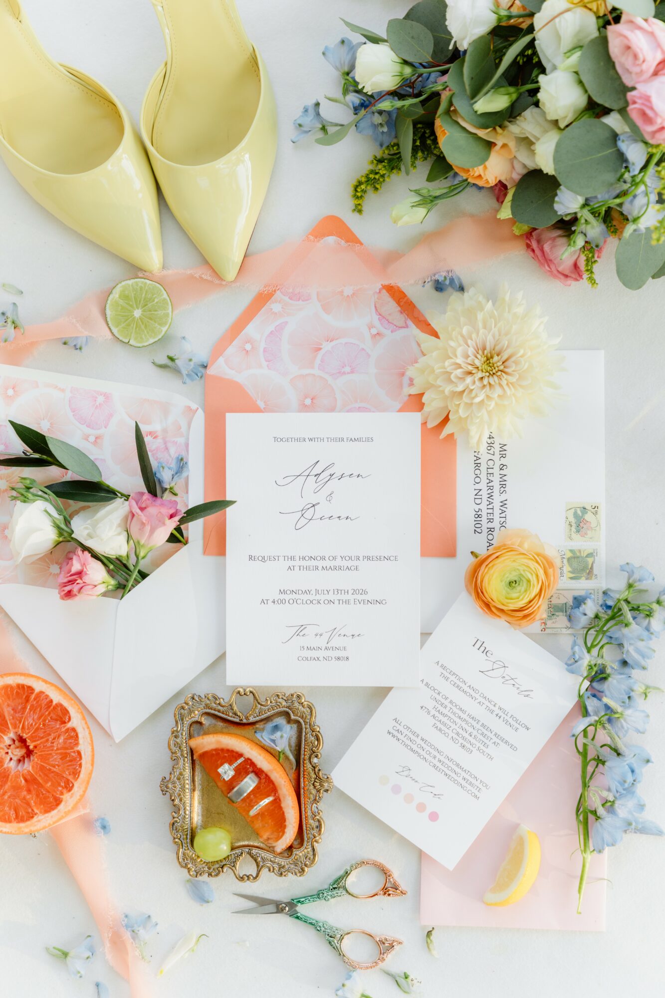 Flat lay of yellow shoes, flowers, citrus fruits, and wedding invitation with decorative elements.