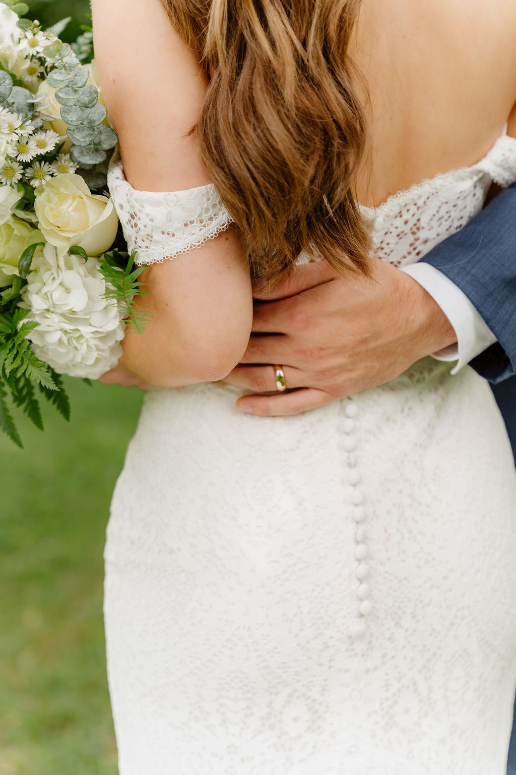 Close-up of a bride and groom embracing, bride holding a bouquet, bride's back, wedding dress, groom's hand on bride's waist