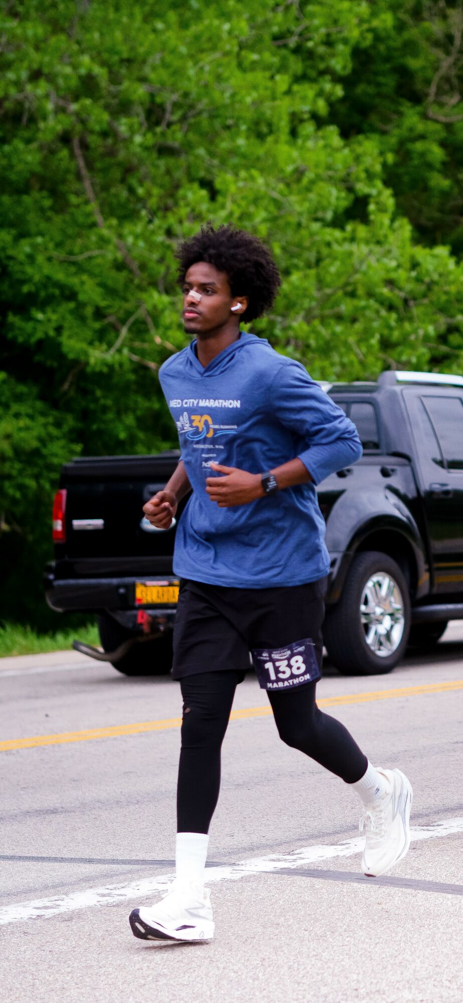 Young person running outdoors with trees and parked cars in background.
