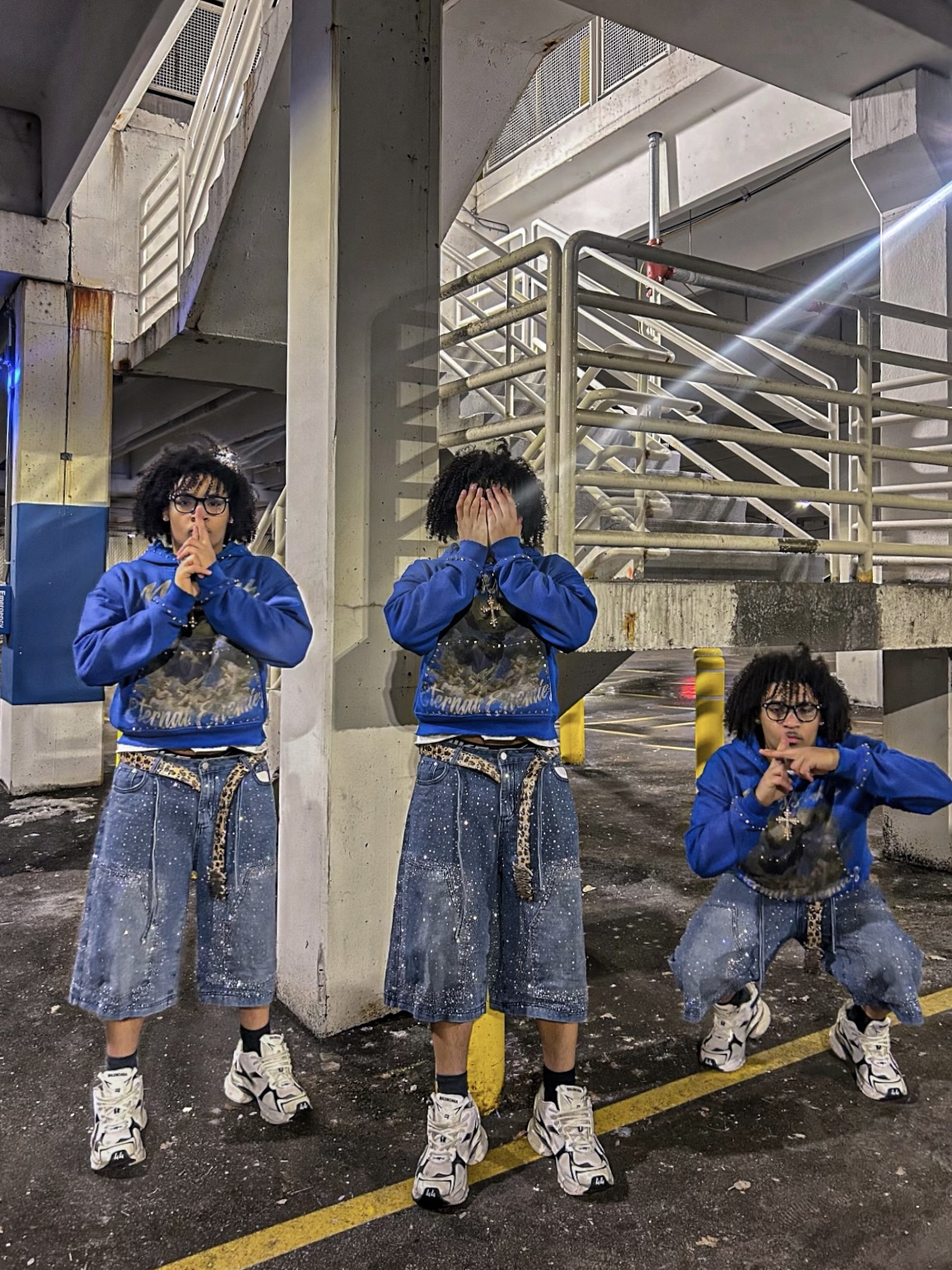 Three people with curly hair wearing blue jackets and denim skirts or pants, covering their faces, standing in a parking garage.