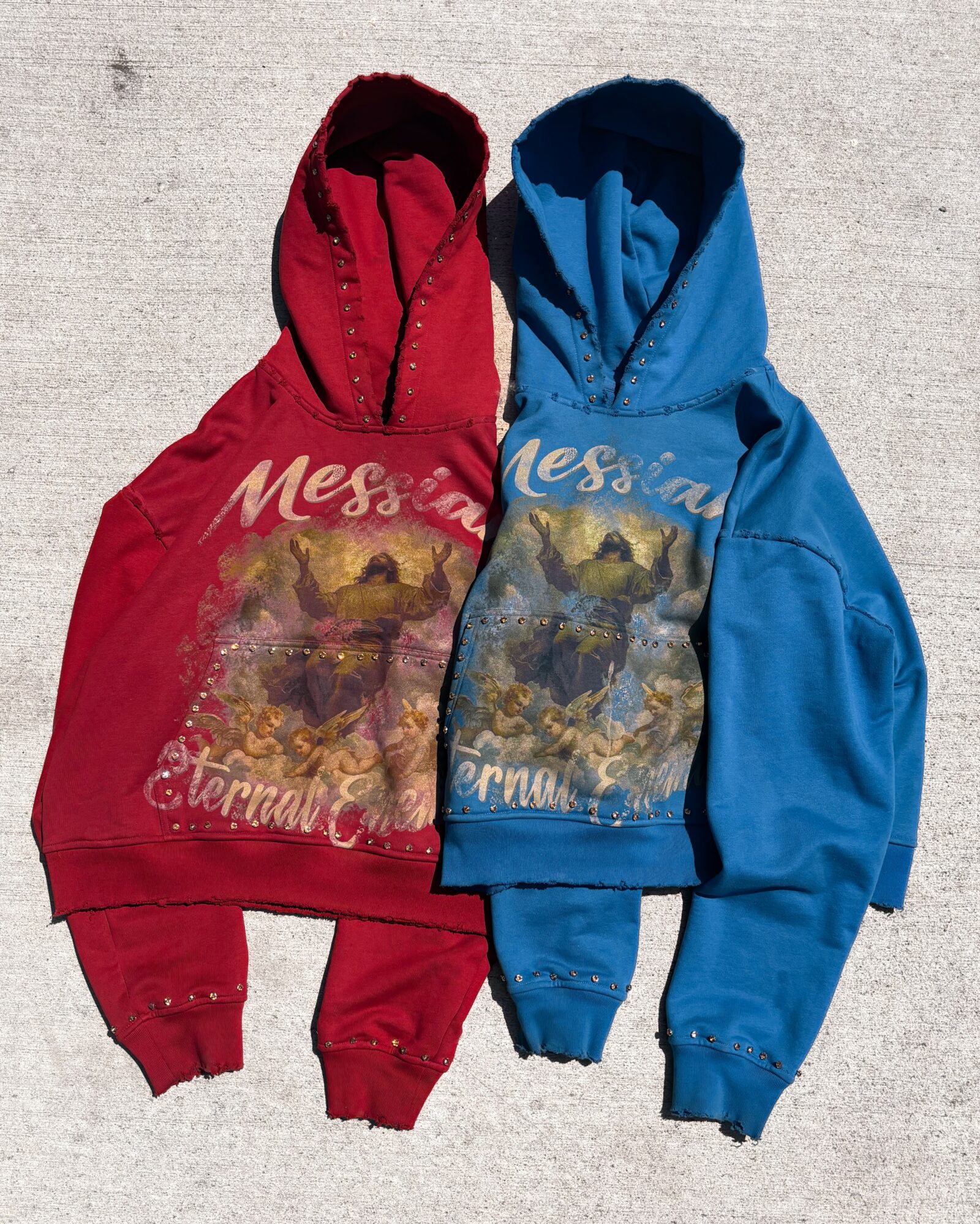 Two hooded sweatshirts, one red and one blue, with mountain landscape prints on the front, laid on a light surface.