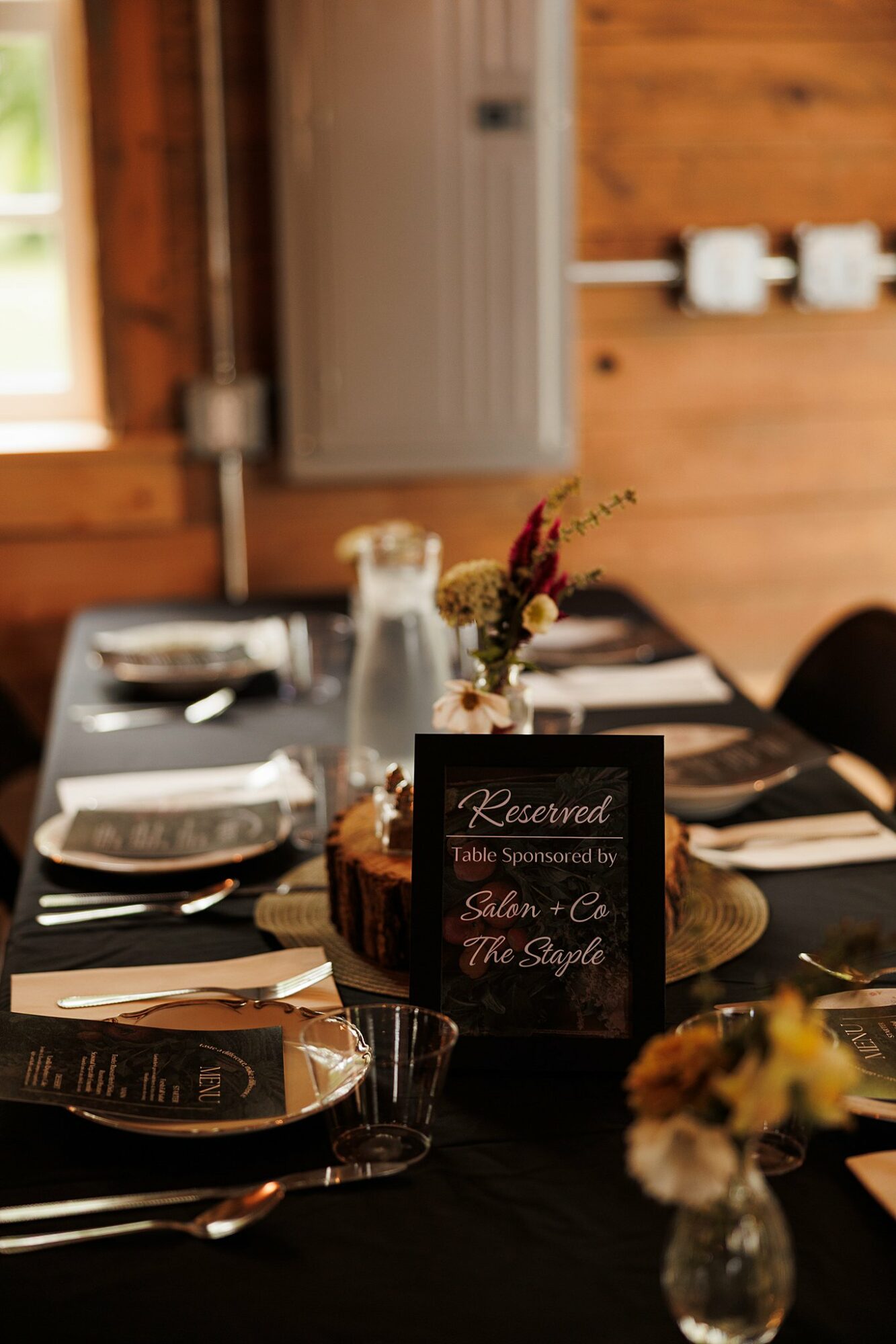 Table setting with plates, glasses, and a floral centerpiece, with a reserved sign in the center, in a wooden room.