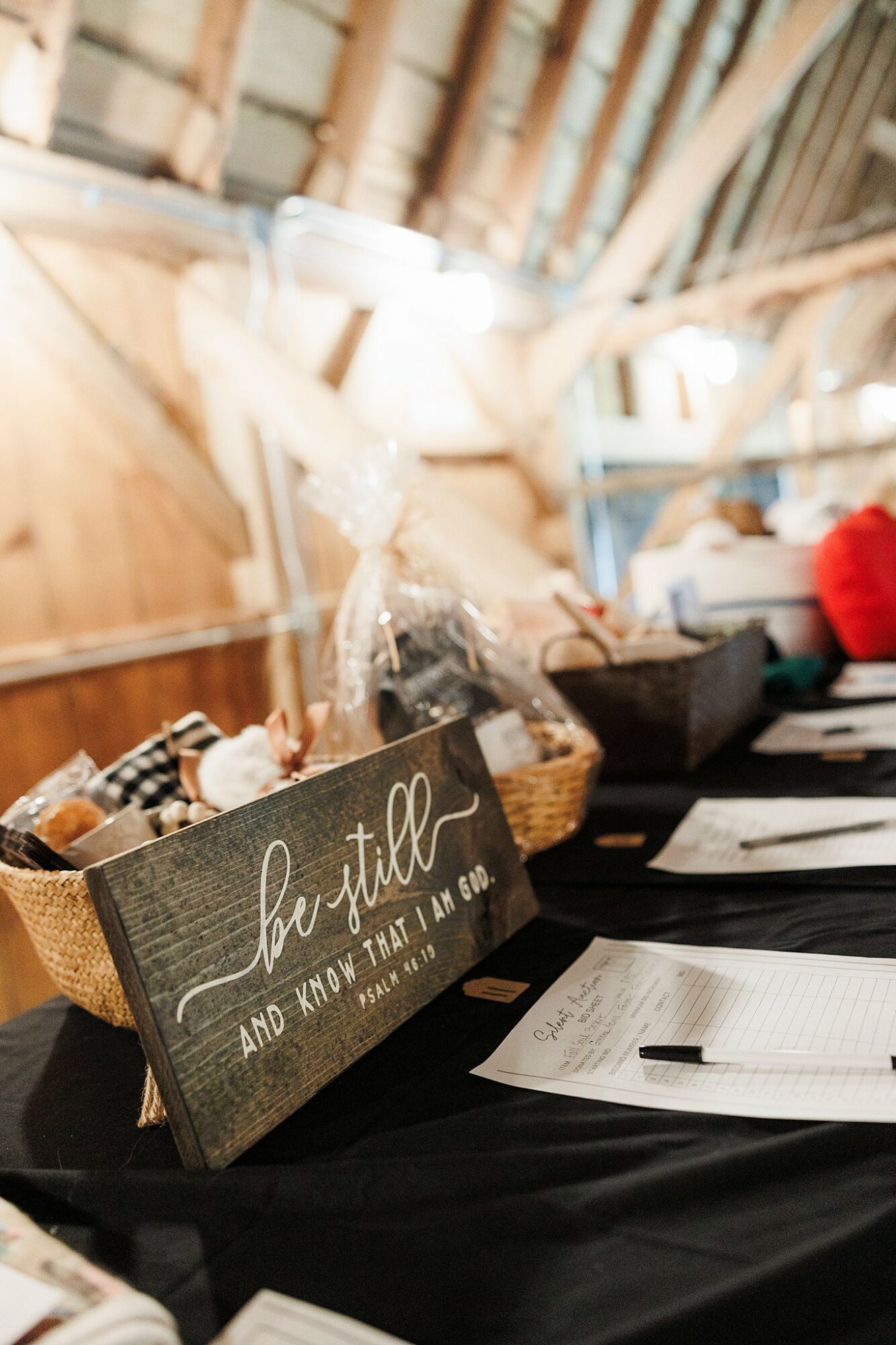 A table with a black sign reading 'be still and know that I am God,' a notebook, and a basket with items inside, in a rustic setting.
