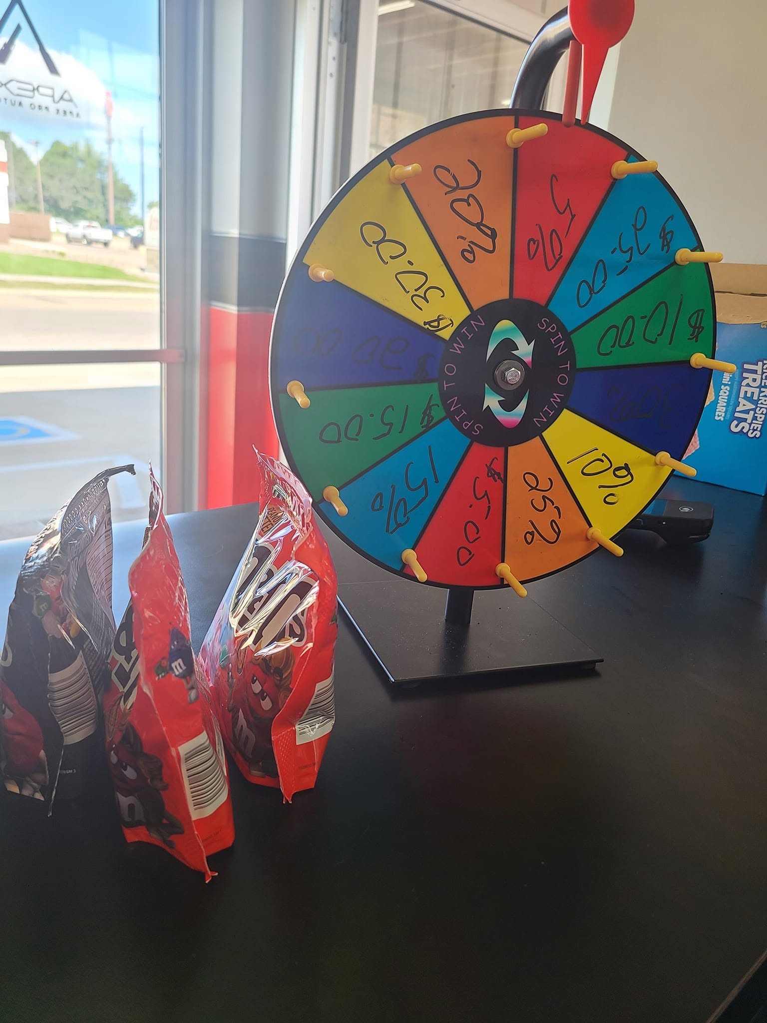 Colorful prize wheel with sections labeled with different prizes, placed on a table near a window.