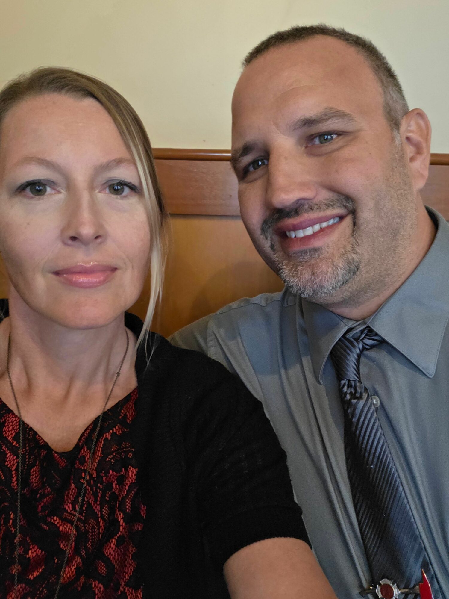 Two people smiling, one woman and one man, in a close-up selfie indoors.