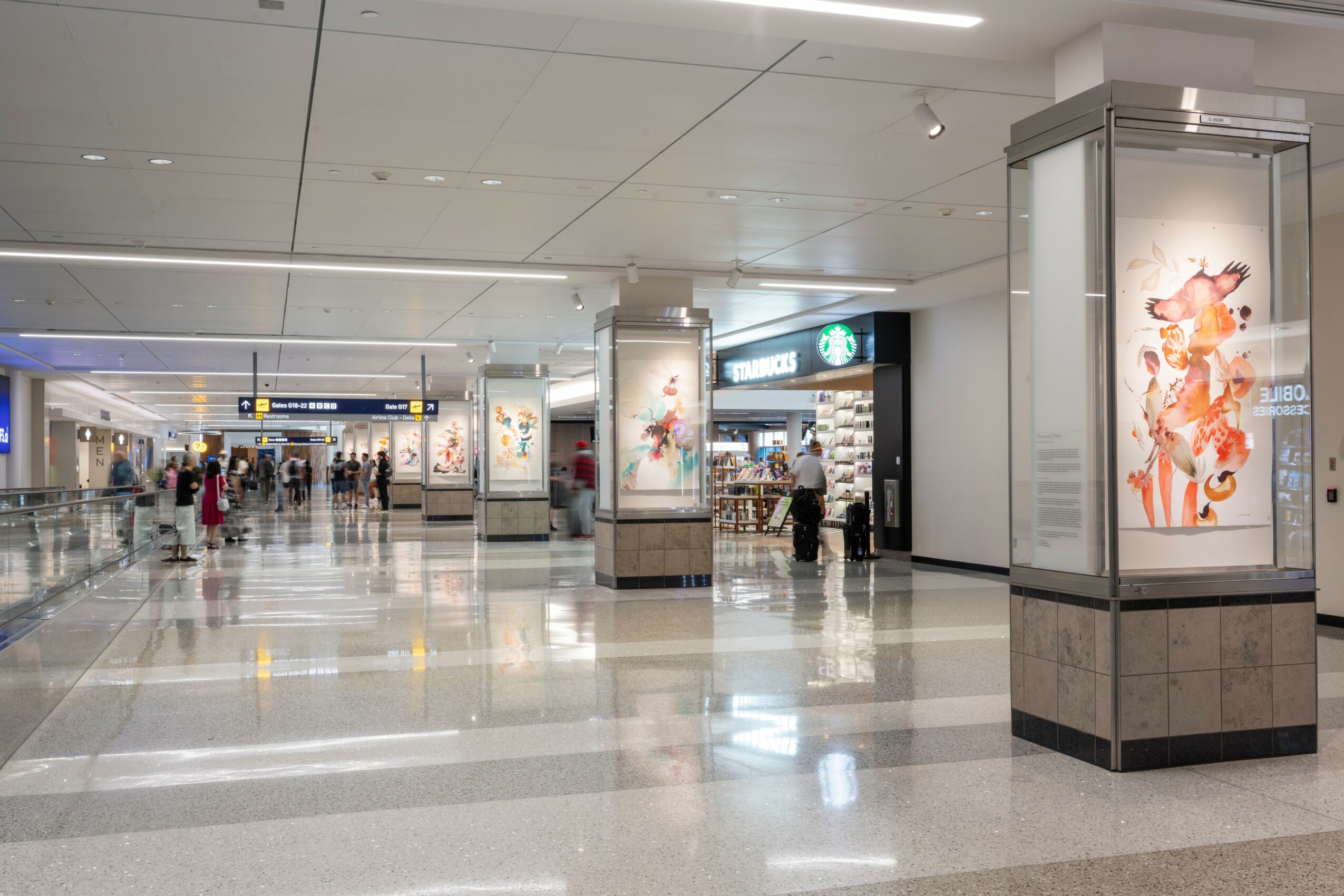 Airport terminal with people walking, illuminated advertisements, and shops, with a shiny floor and ceiling lights.