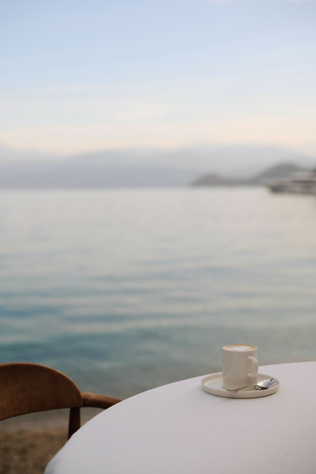 A table with a cup and saucer near a body of water, with a distant shoreline and sky in the background.