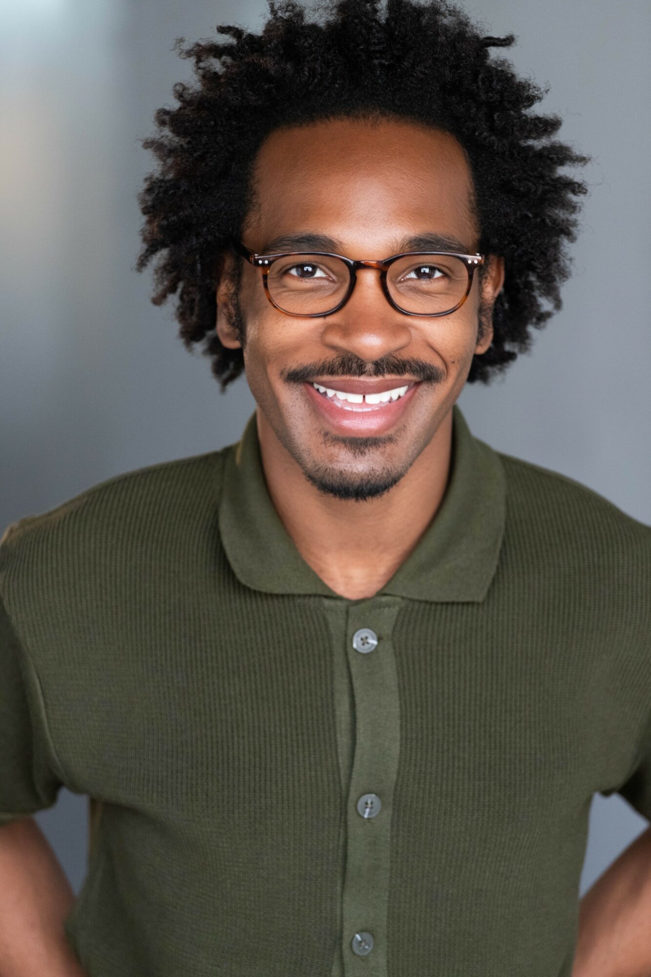 Smiling man with glasses and curly hair wearing a green polo shirt, facing forward.