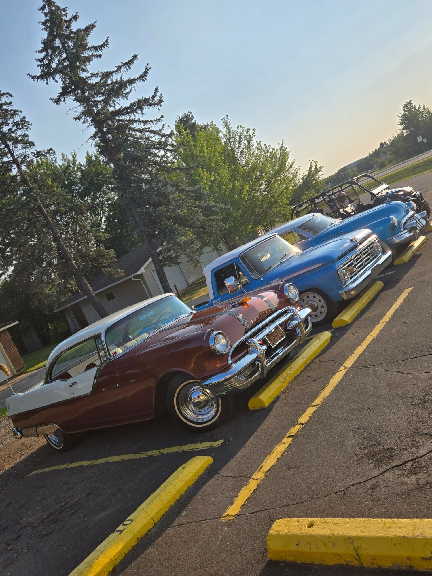 Cars parked in a lot with trees in the background, viewed from the side, with yellow parking blocks.