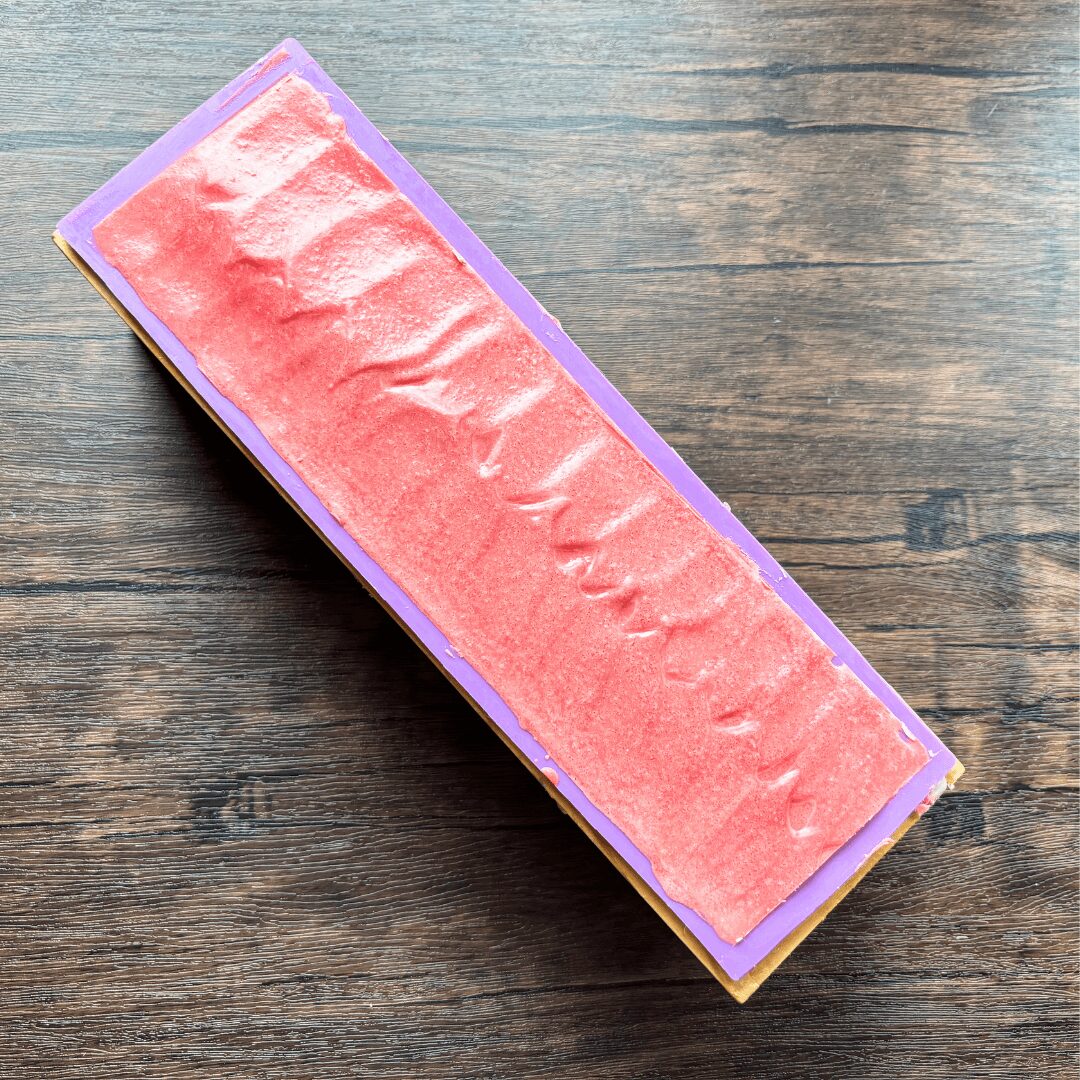 A rectangular box with a pink textured surface on a wooden table, viewed from an angle.
