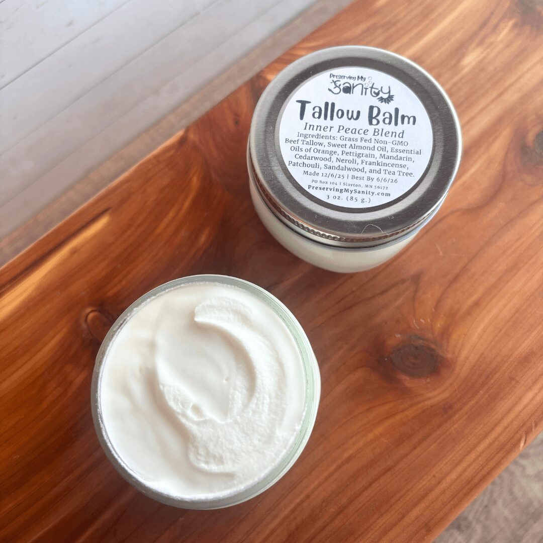 Open jar of Tallow Balm with white cream inside on wooden surface, lid with label visible, top view.