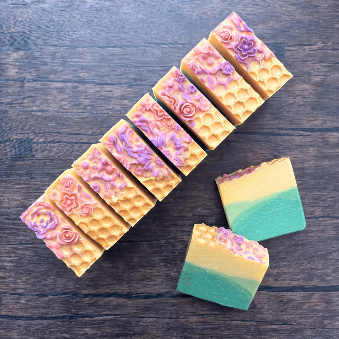 Six soap bars with floral and swirl patterns, two layered soaps with pastel colors, on a wooden surface.