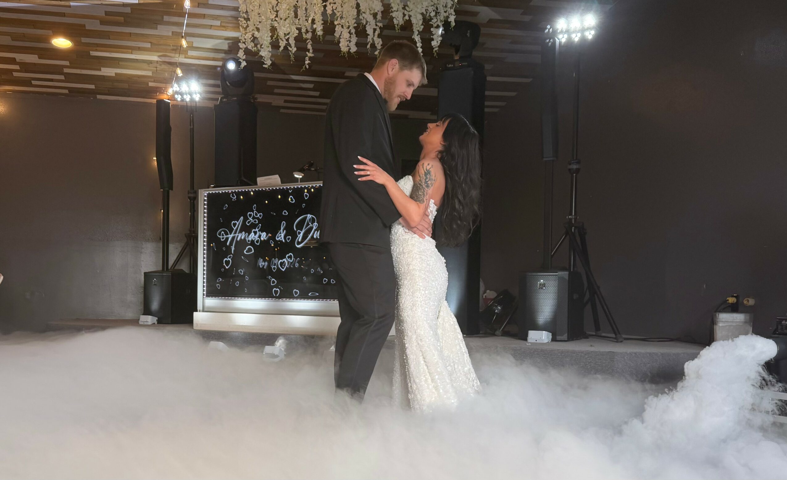 A couple dancing on a foggy dance floor with a dark background and decorative lighting.
