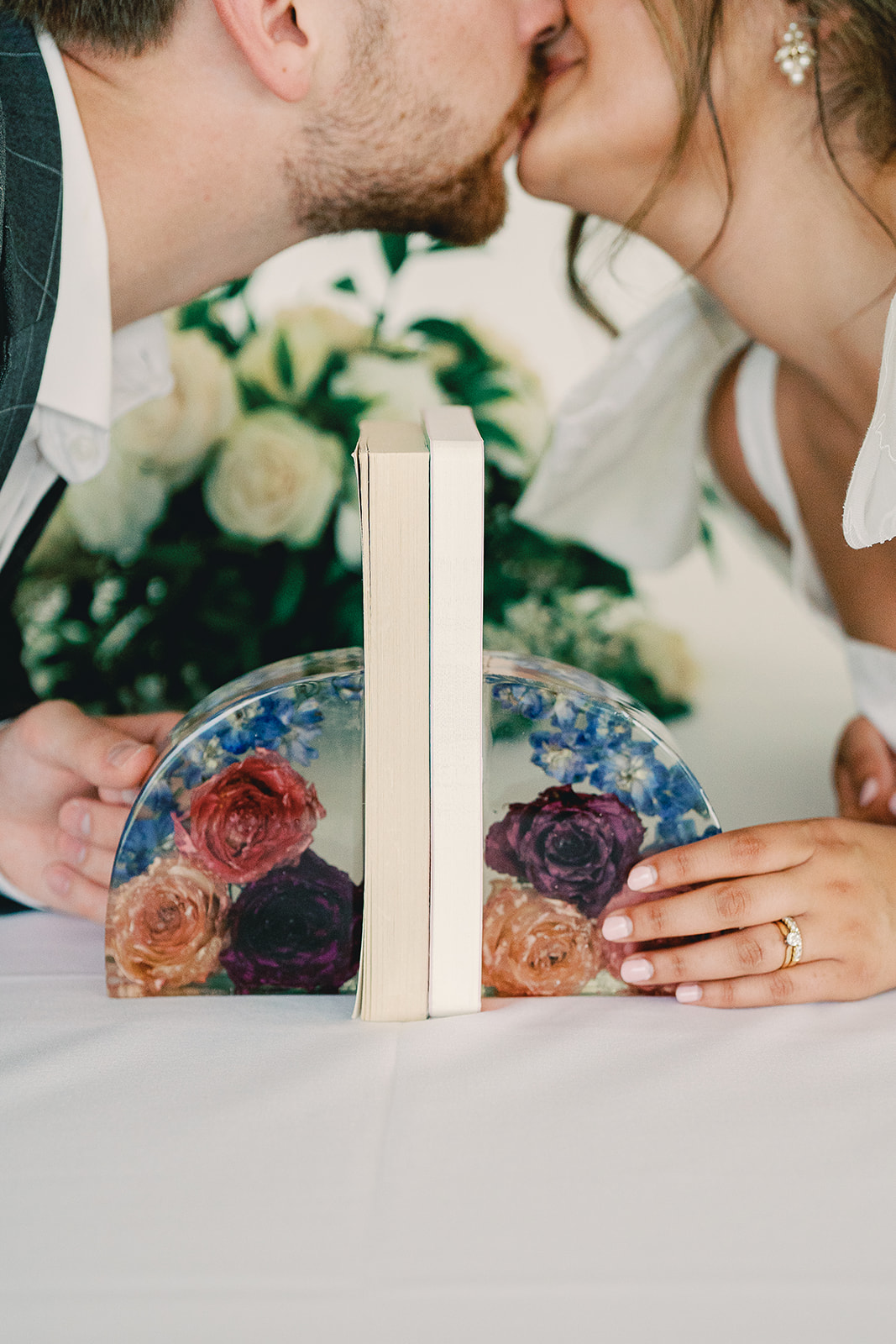 Couple kissing at a wedding with a decorative cake and flowers in the background.