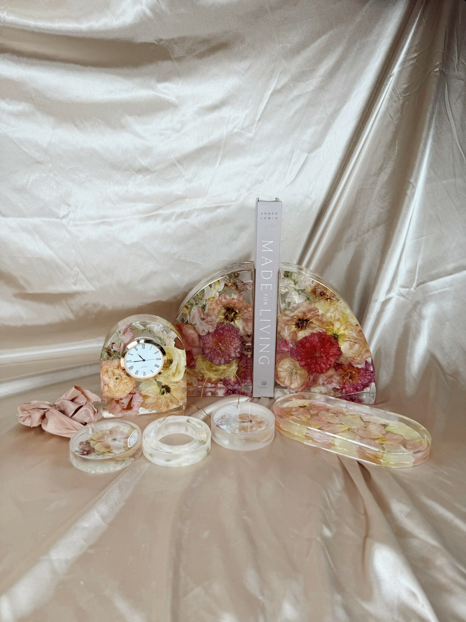 Various soap bars and a ruler on a silky fabric background, with a large soap embedded with flowers and smaller soap pieces.