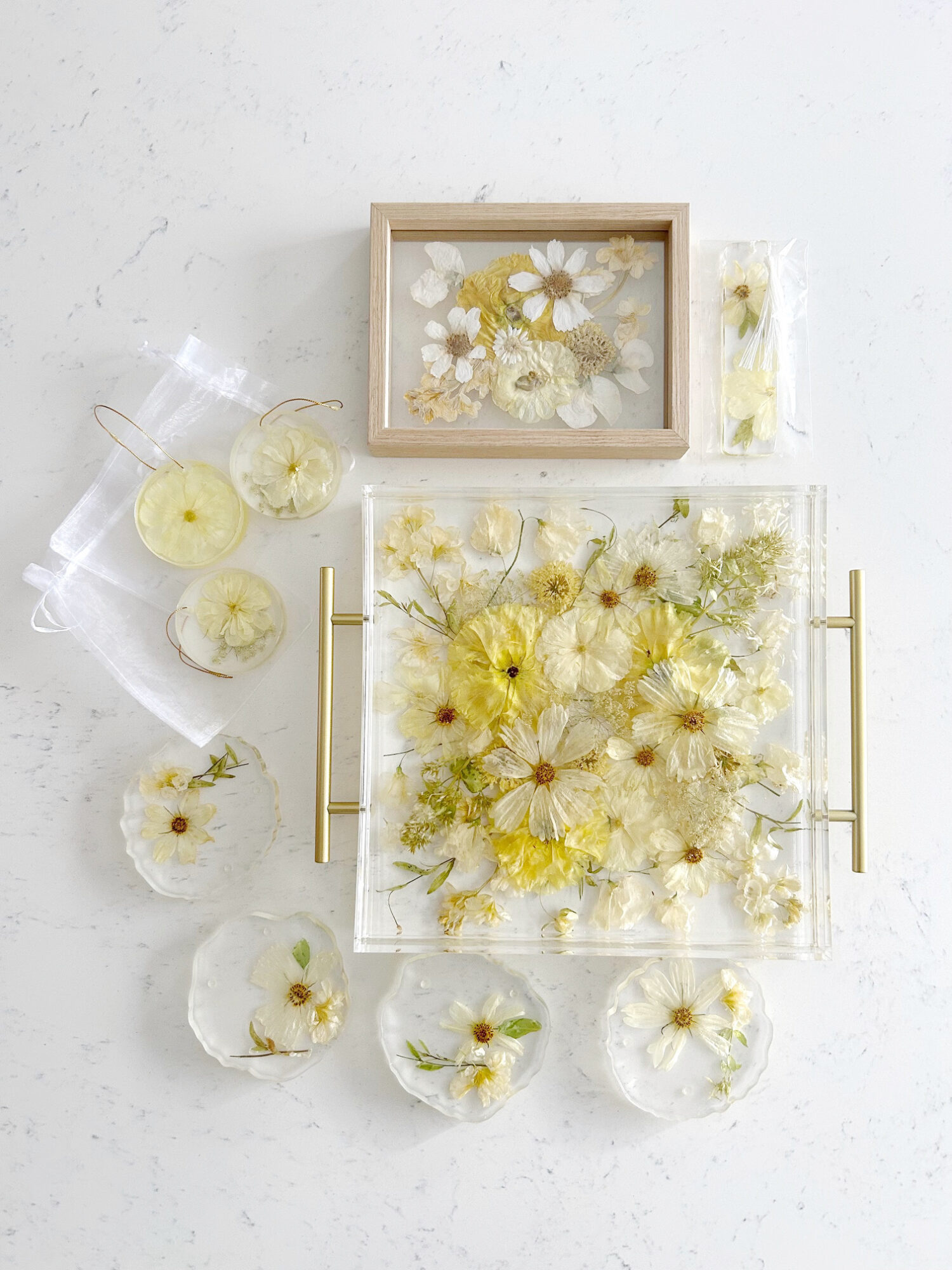 Flat lay of dried flowers in glass containers and a wooden box on a white surface.