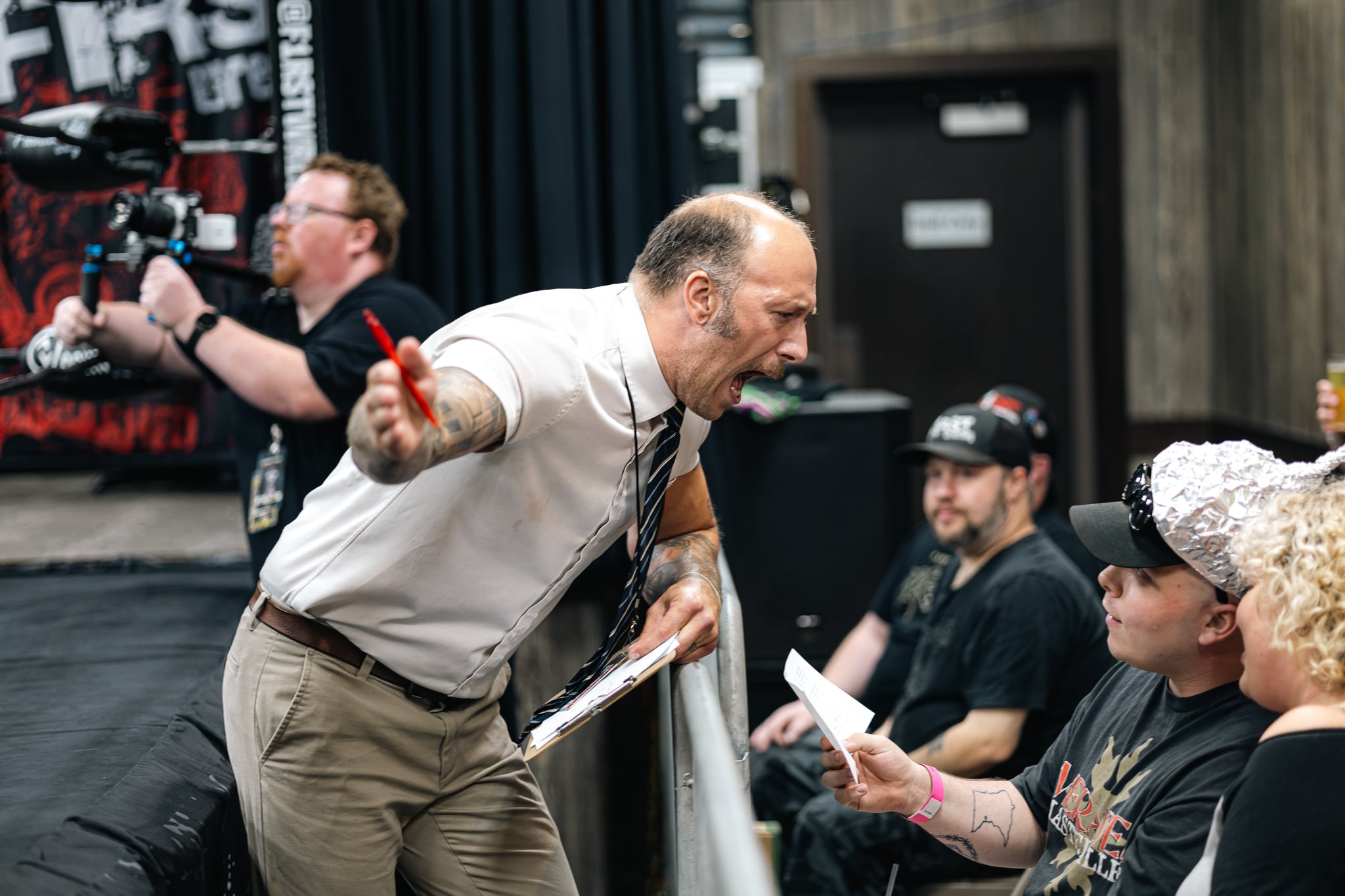 Man shouting and gesturing passionately at a group of people in an indoor setting.
