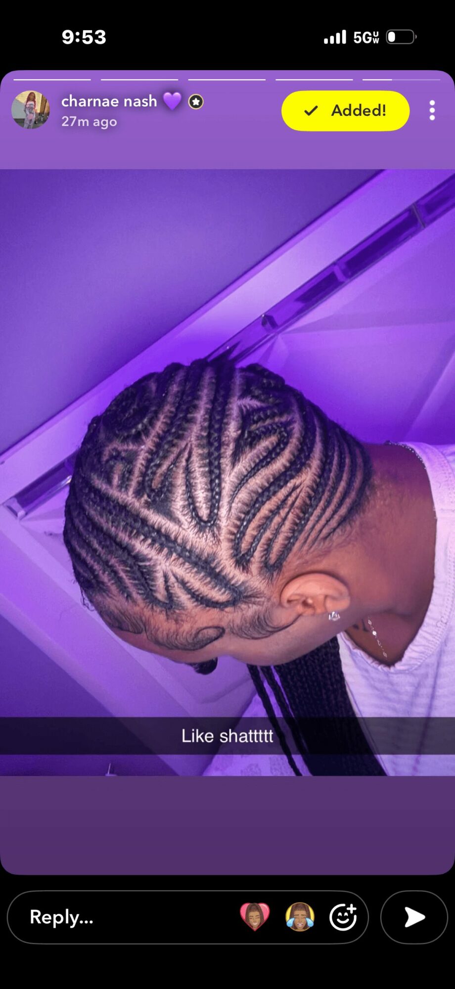Person with intricate braided hairstyle illuminated by purple lighting, facing downward, with a white shirt visible.