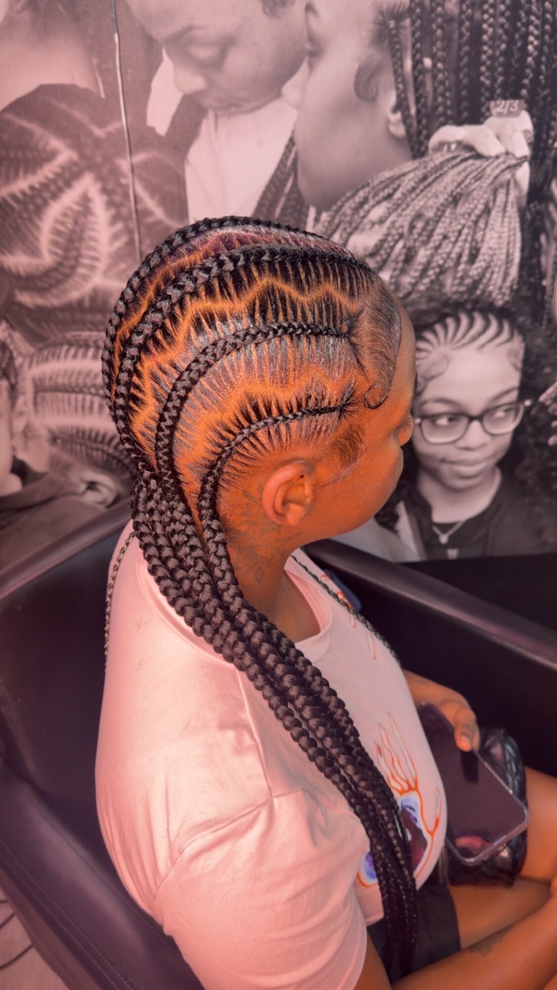 Child with braided hairstyle sitting on a seat, wearing a light-colored top, in front of a black-and-white photo background.
