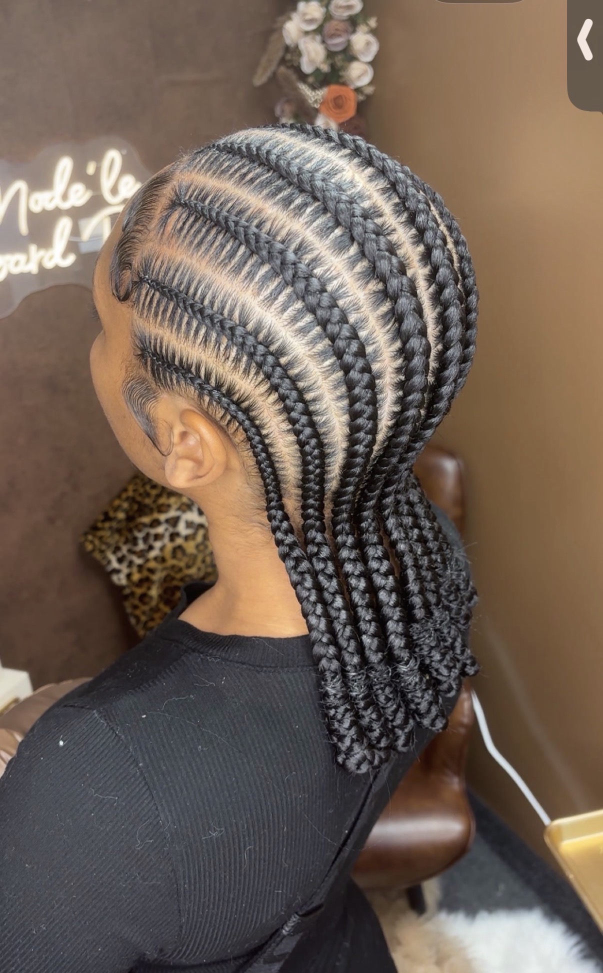 Side view of a person with intricately braided hair styled in a pattern, wearing a black top, in a room with decor.
