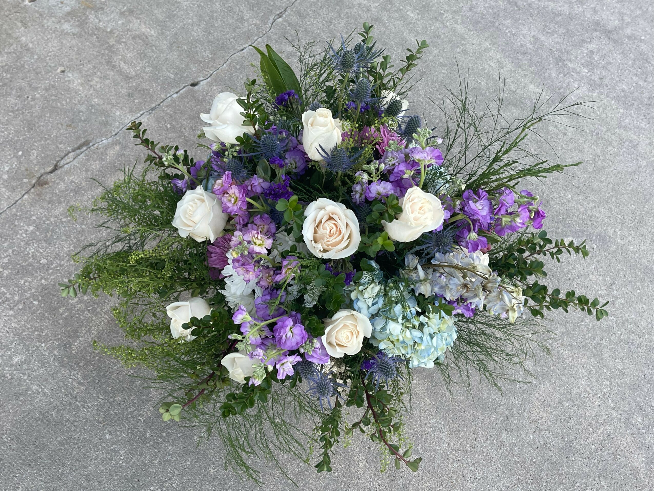 Flower arrangement with white, purple, and blue flowers and green foliage on a gray surface.
