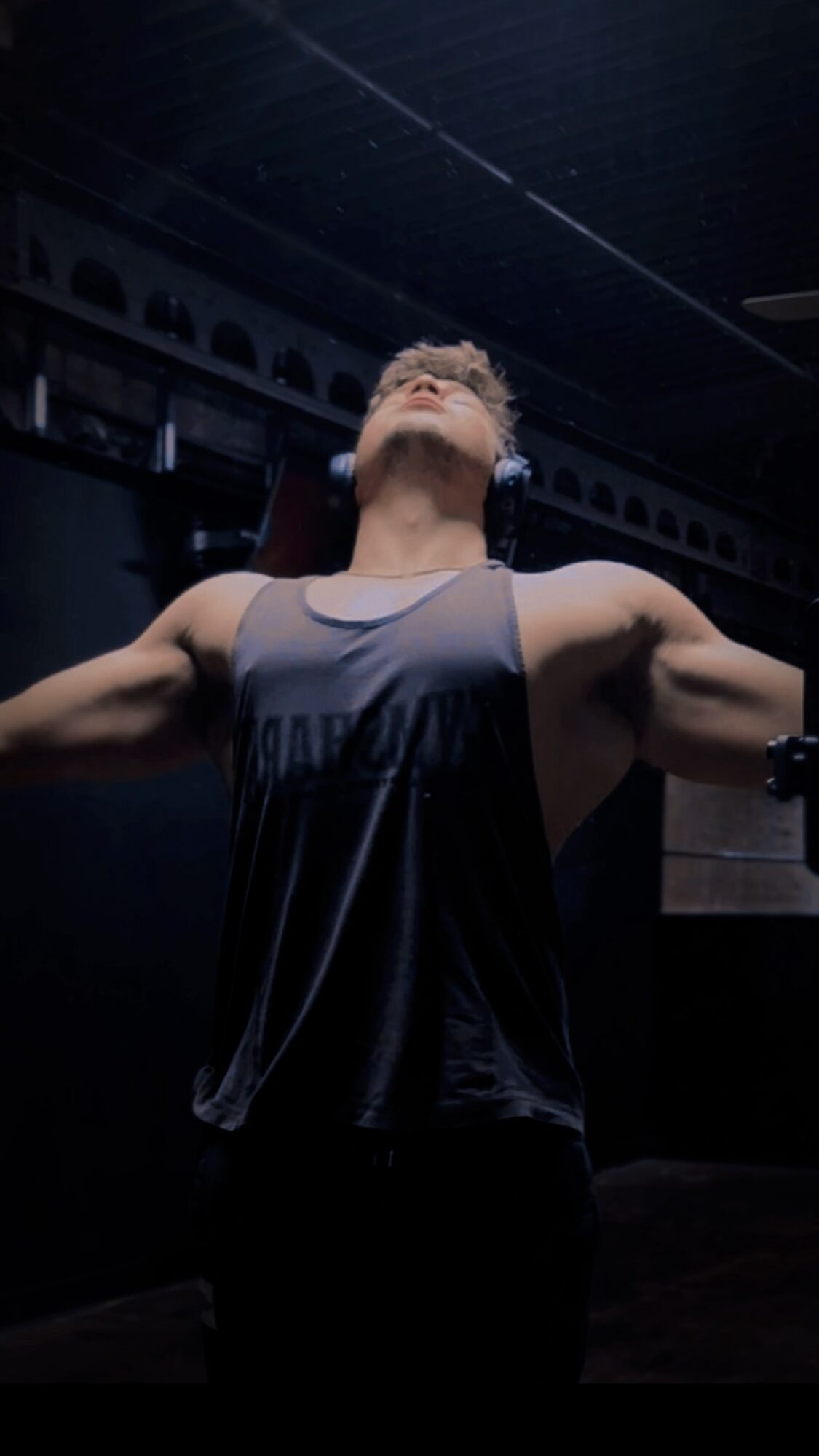 Person with arms outstretched, head tilted back, in a dark room with high ceiling and architectural details.