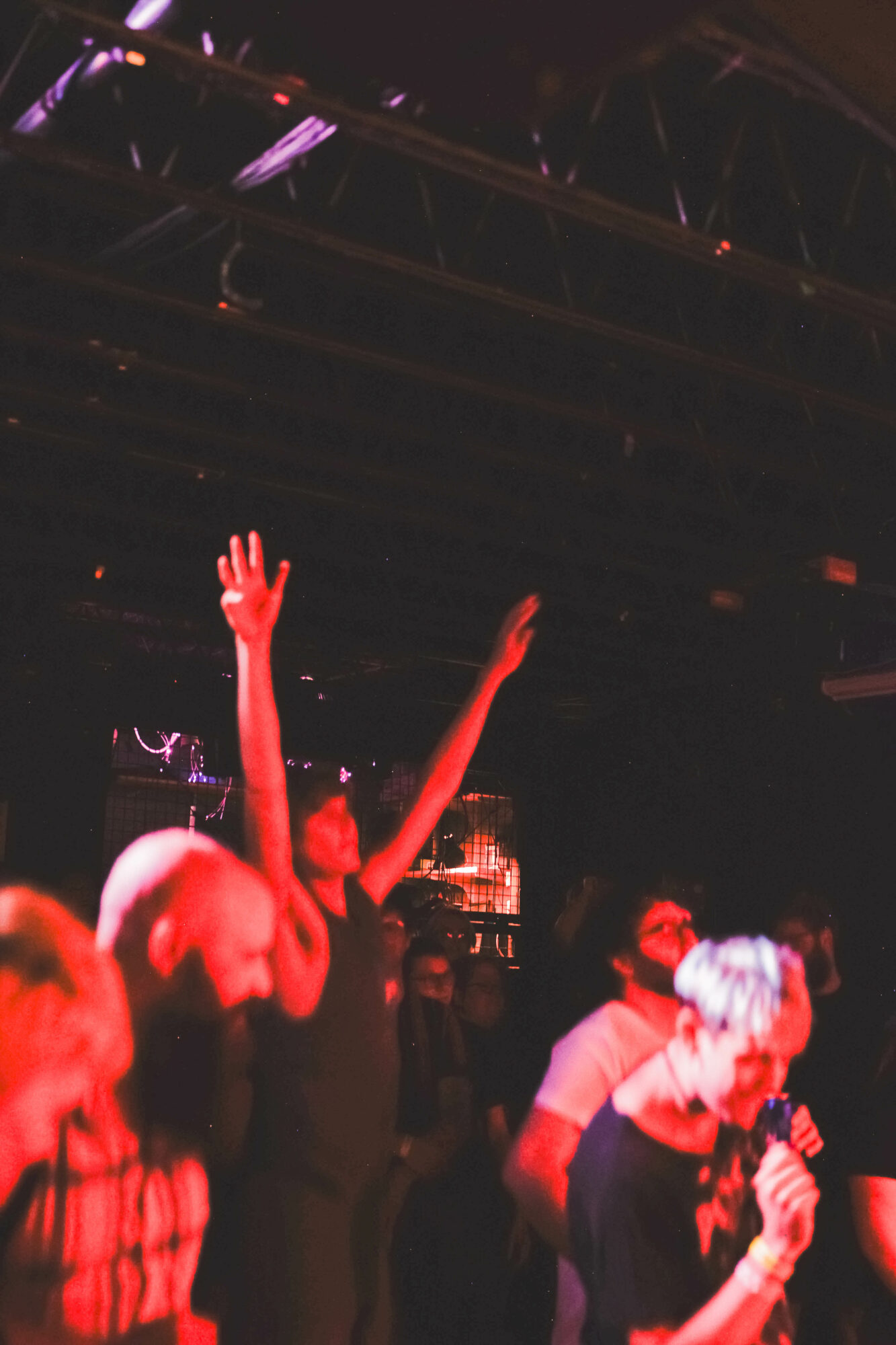 People at a concert with one person raising hands, others dancing, in a dark environment with colorful lighting.