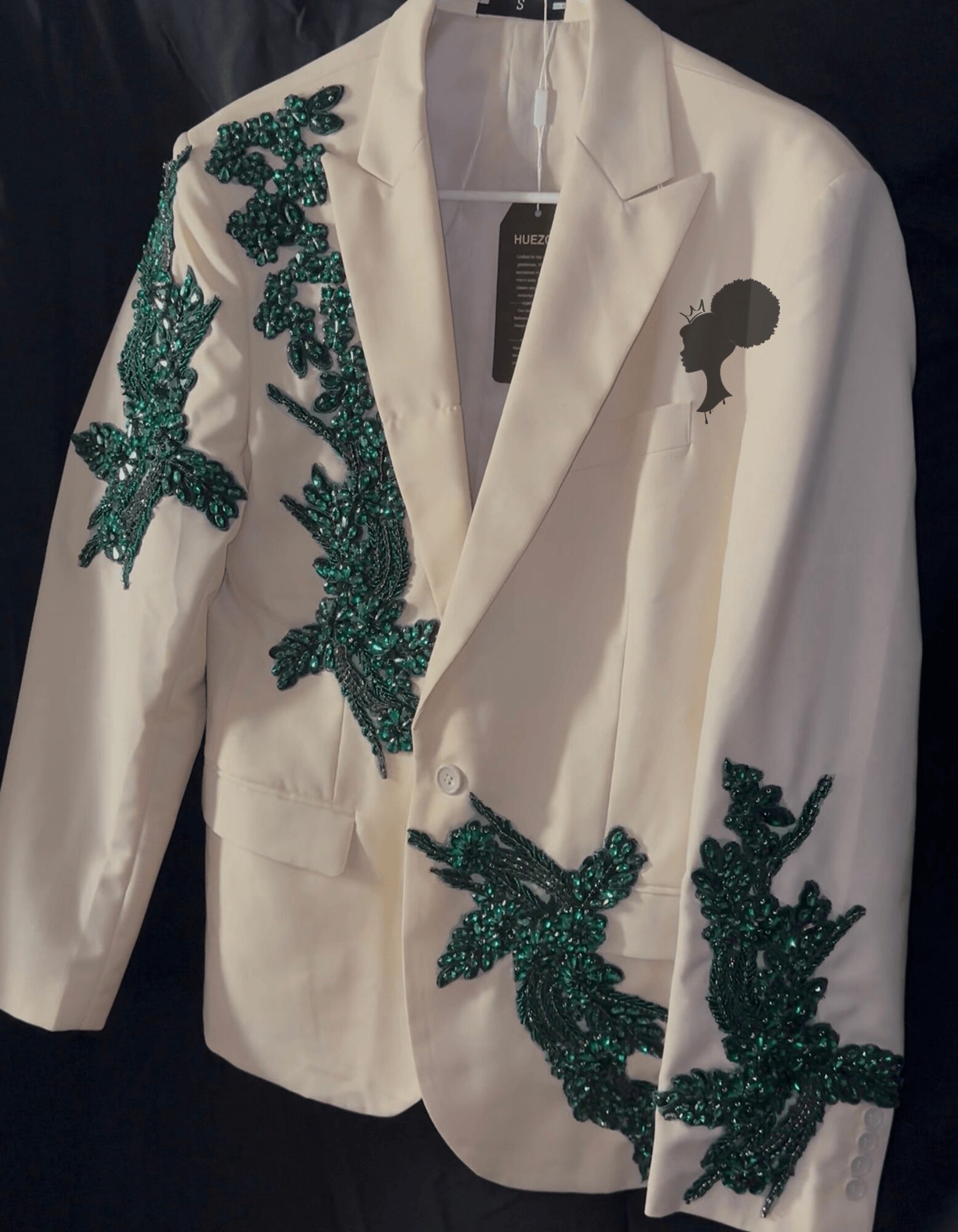 White blazer with green beaded floral embroidery on the left shoulder and lower right side, and a small black silhouette on the chest.
