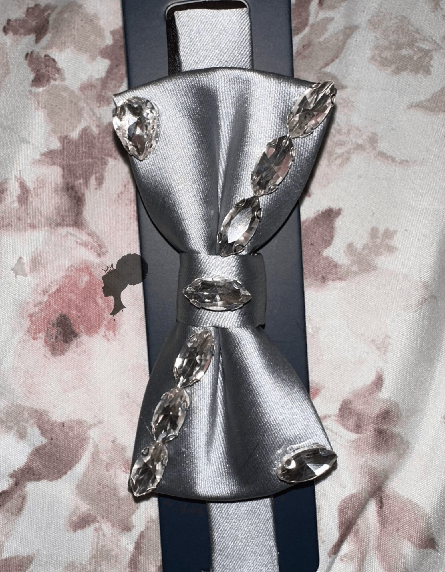 Silver bow-shaped accessory with clear gemstones on a dark background, on a floral fabric surface.