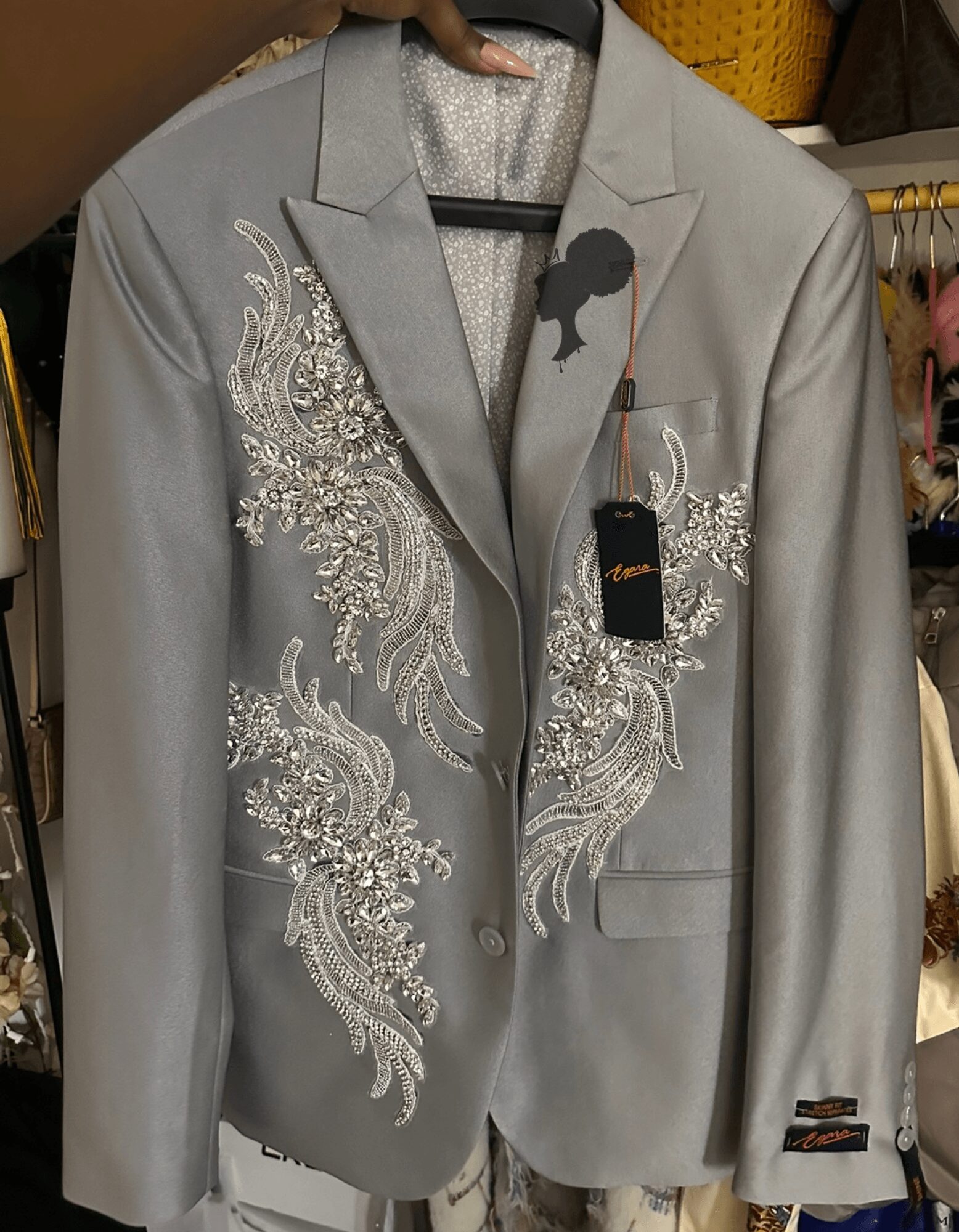 Gray blazer with embroidered white floral patterns on front, hanging on a black hanger in a clothing store.