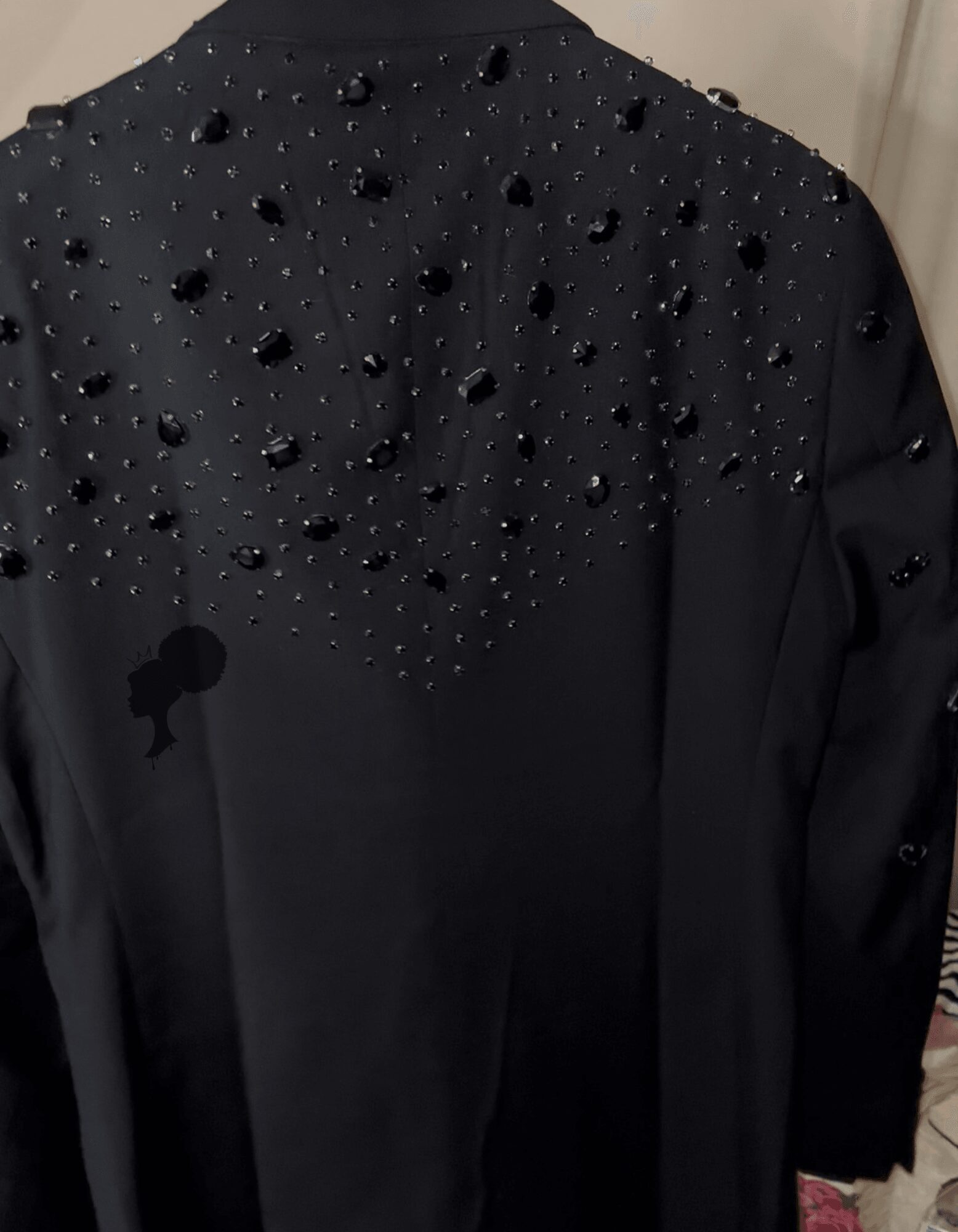 Black garment with decorative black beads or embellishments on the upper part, possibly a jacket or dress, with a plain background.